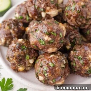 A plate of cooked meatballs mixed with chopped spinach, herbs, and cheese, arranged closely together on a white dish.