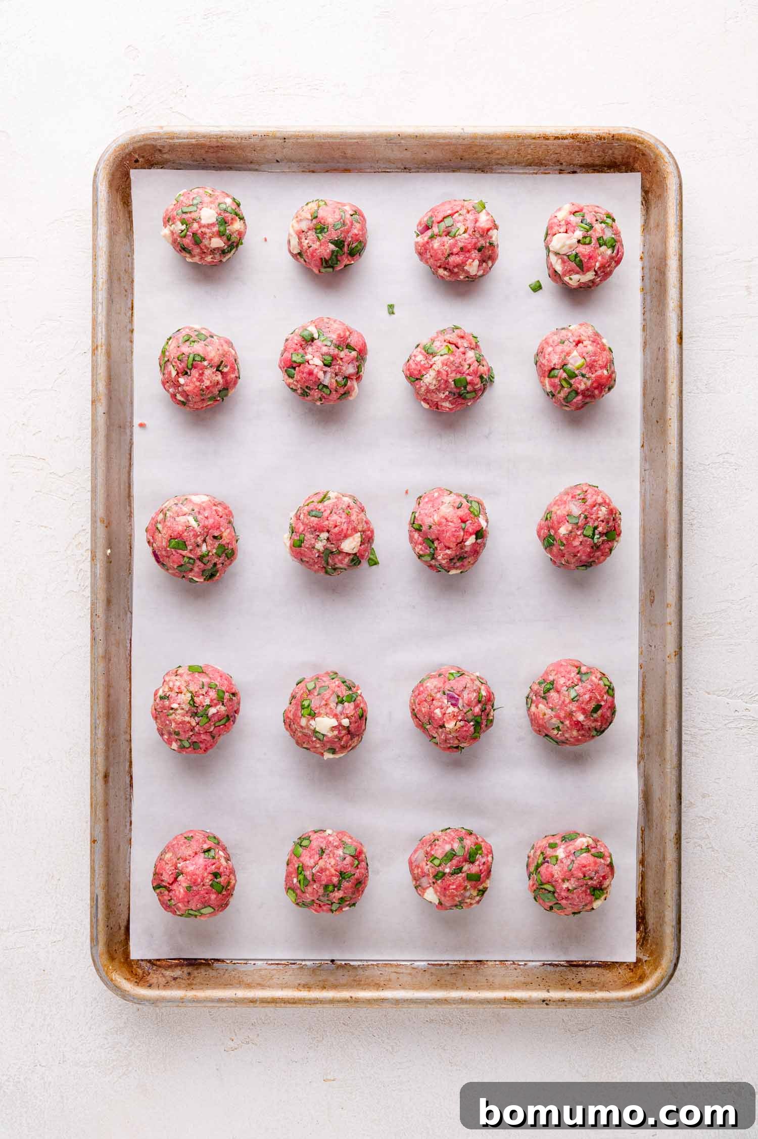 Uncooked meatballs are arranged in rows on a parchment-lined baking sheet.