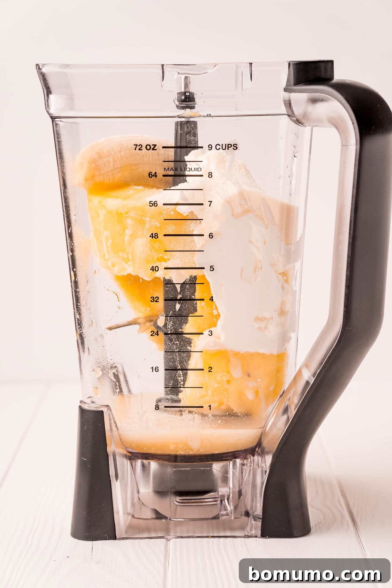 Pineapple Paradise Smoothie 4 A blender pitcher containing scoops of yellow pineapple and white yogurt, with measurements marked on the side, sits on a white surface.