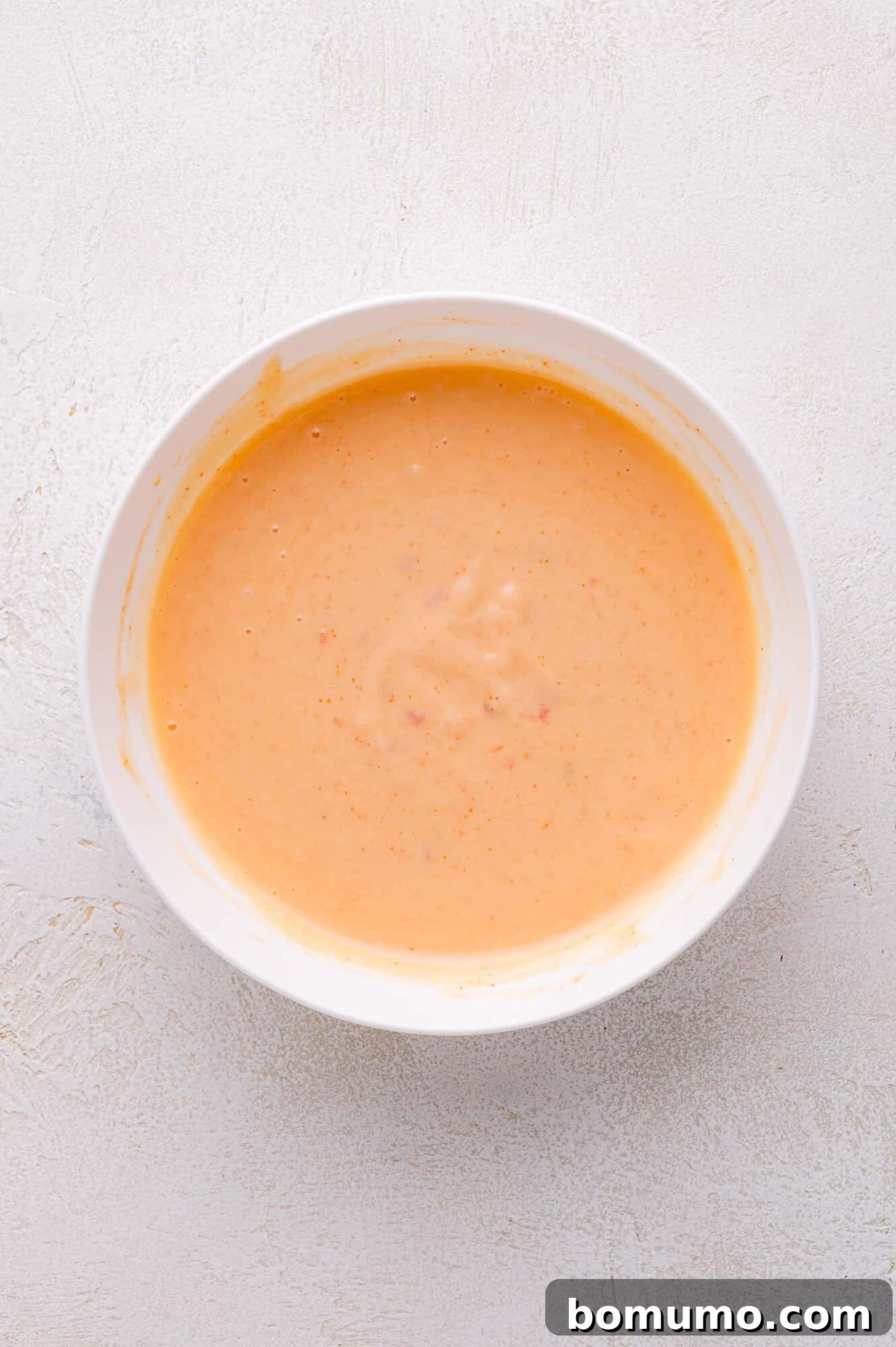 Sweet Chili Blast 6 A pristine white bowl is filled to the brim with a luxuriously creamy, perfectly orange-colored Bang Bang Sauce, beautifully presented on a light textured surface, ready for dipping or drizzling.