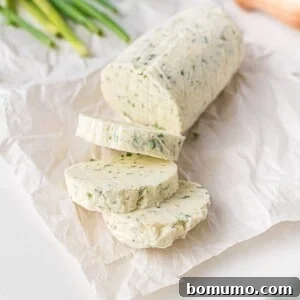 Sliced chive butter log on parchment paper, ready to serve, with fresh chives in the background.