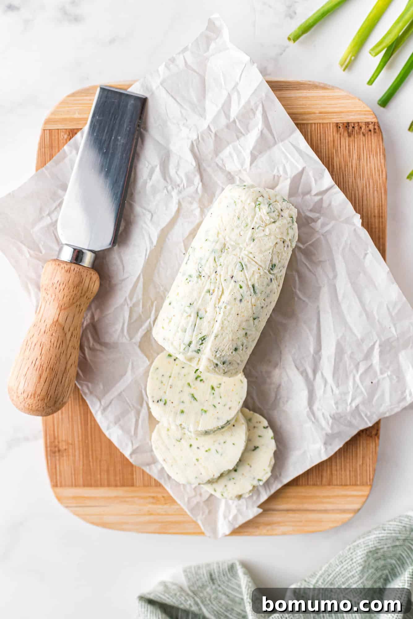 Verdant Chive Butter 7 A perfectly formed, partially sliced log of herb butter on parchment paper, resting on a rustic wooden cutting board, with a elegant butter knife suggesting it's ready for serving.
