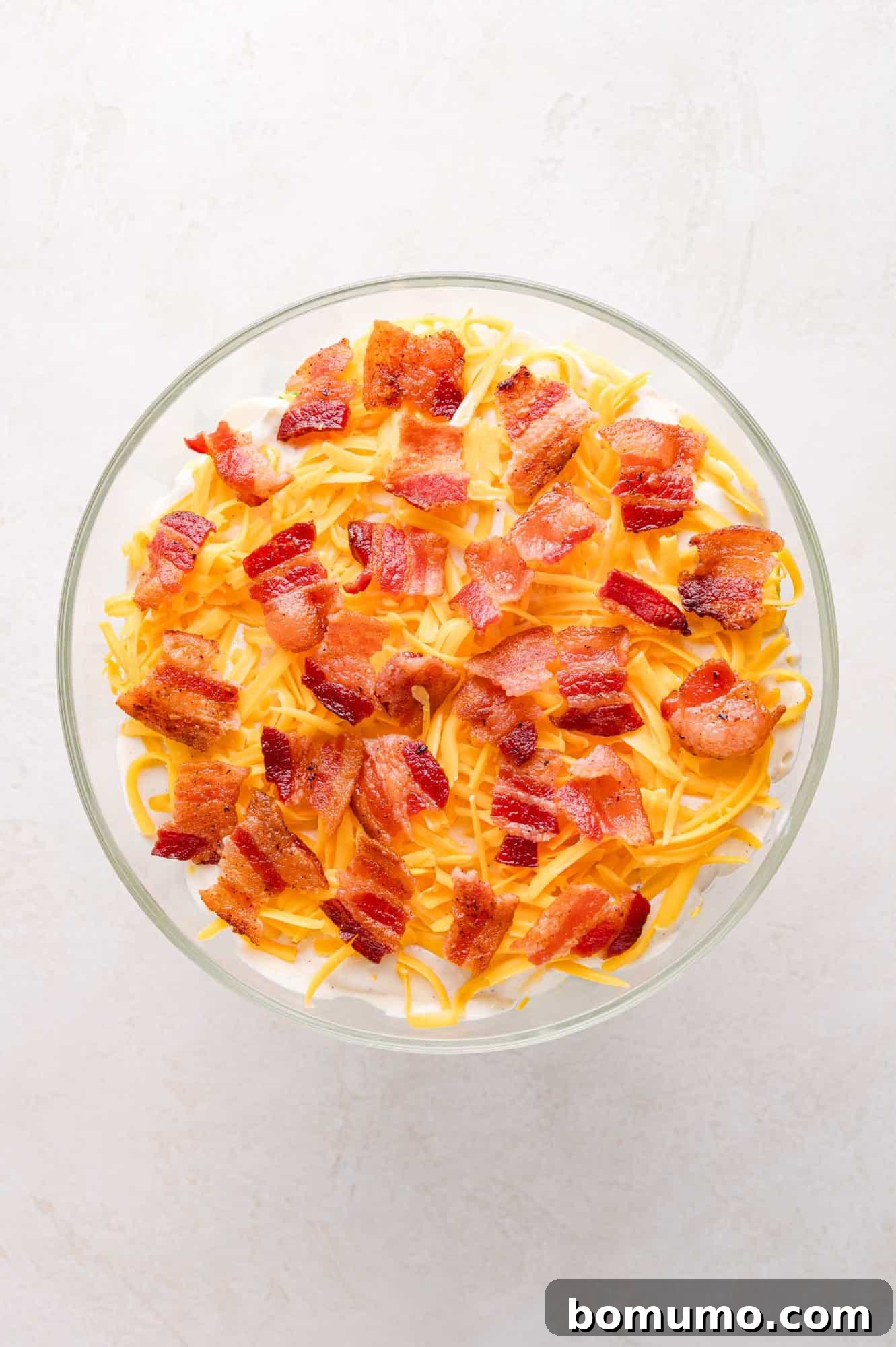 Stacked Garden Bliss 9 A top-down view of the completed seven layer salad, beautifully presented with a visible top layer of golden cheddar cheese and crispy bacon bits, ready for serving.
