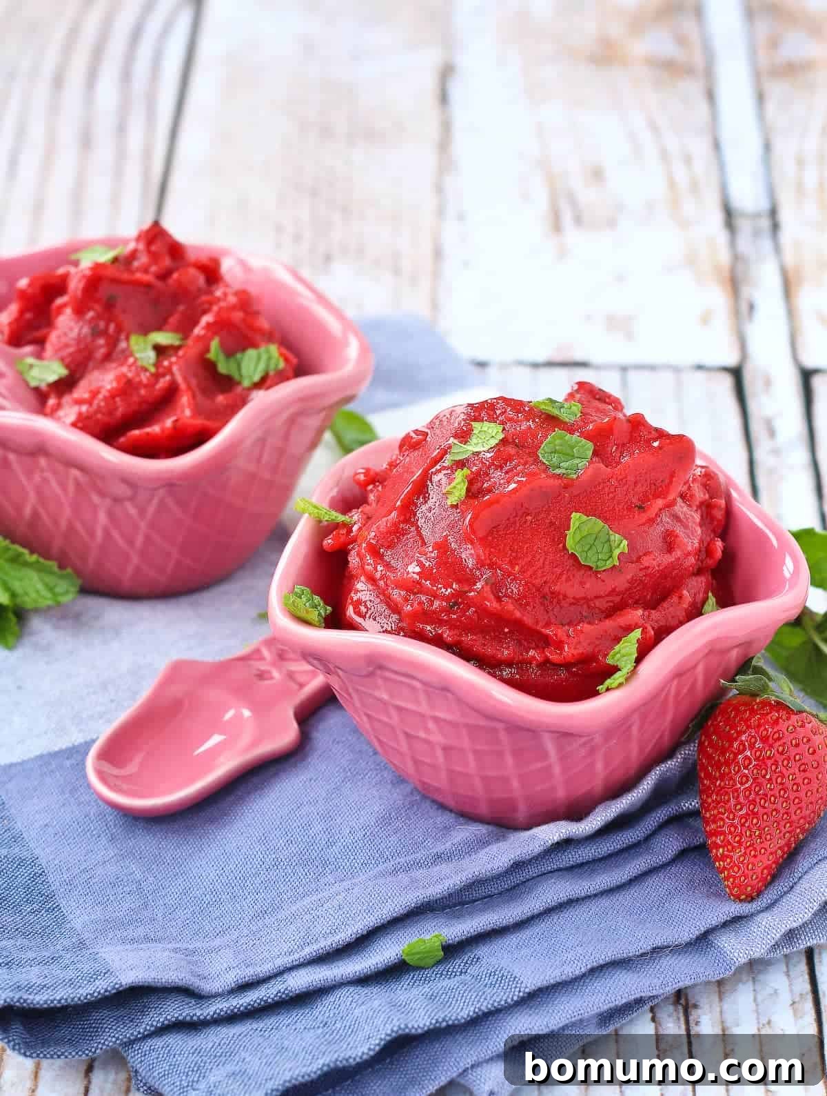 Two pink bowls filled with vibrant strawberry mint sorbet, garnished with fresh green mint leaves, ready to be enjoyed.