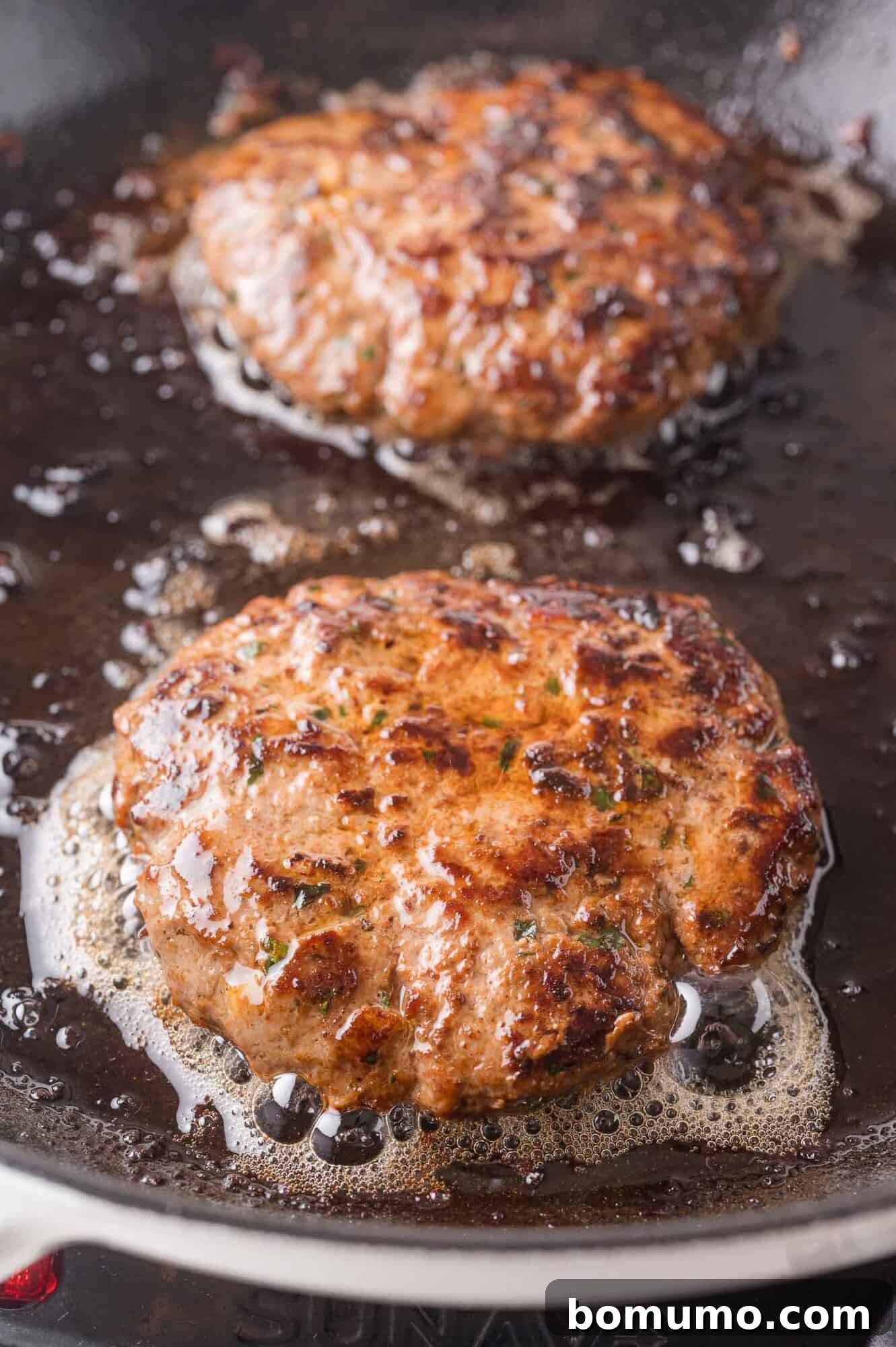 Two browned ground lamb patties sizzling in a frying pan with bubbling oil.