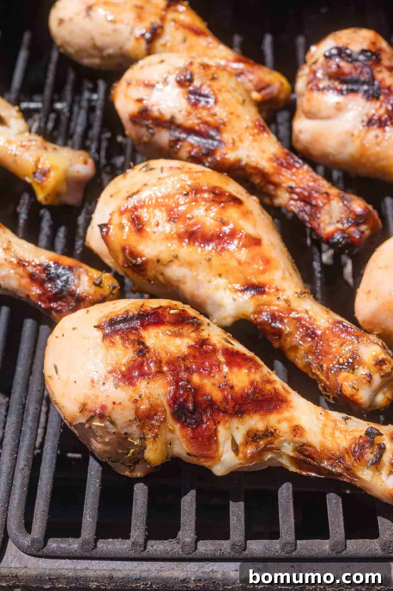 Grilled chicken drumsticks cooking on a barbecue grill, with beautiful char marks visible on the meat.