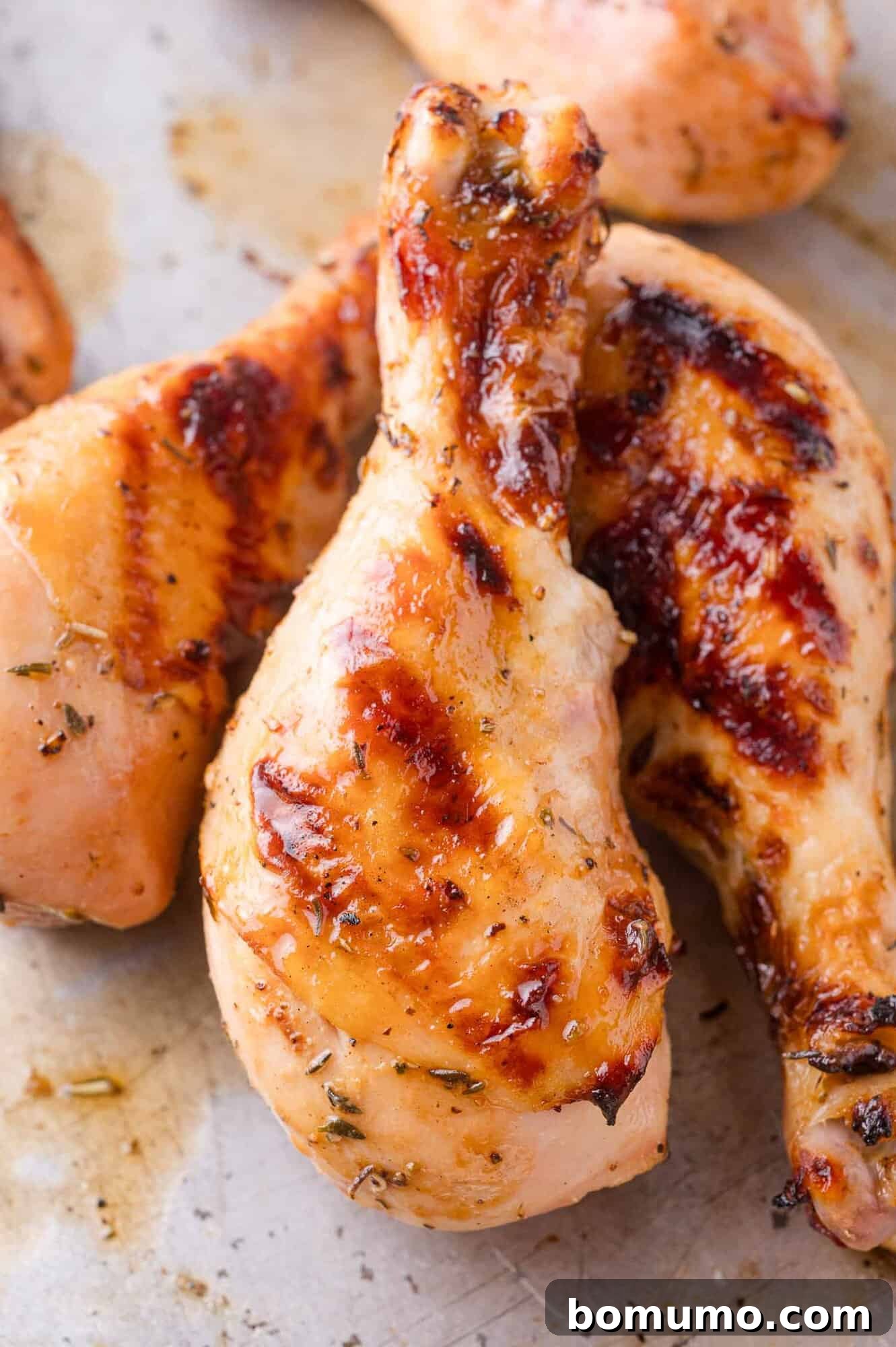 Close-up of perfectly grilled chicken drumsticks with a golden brown, slightly glazed skin on a metal baking sheet, ready for garnish.