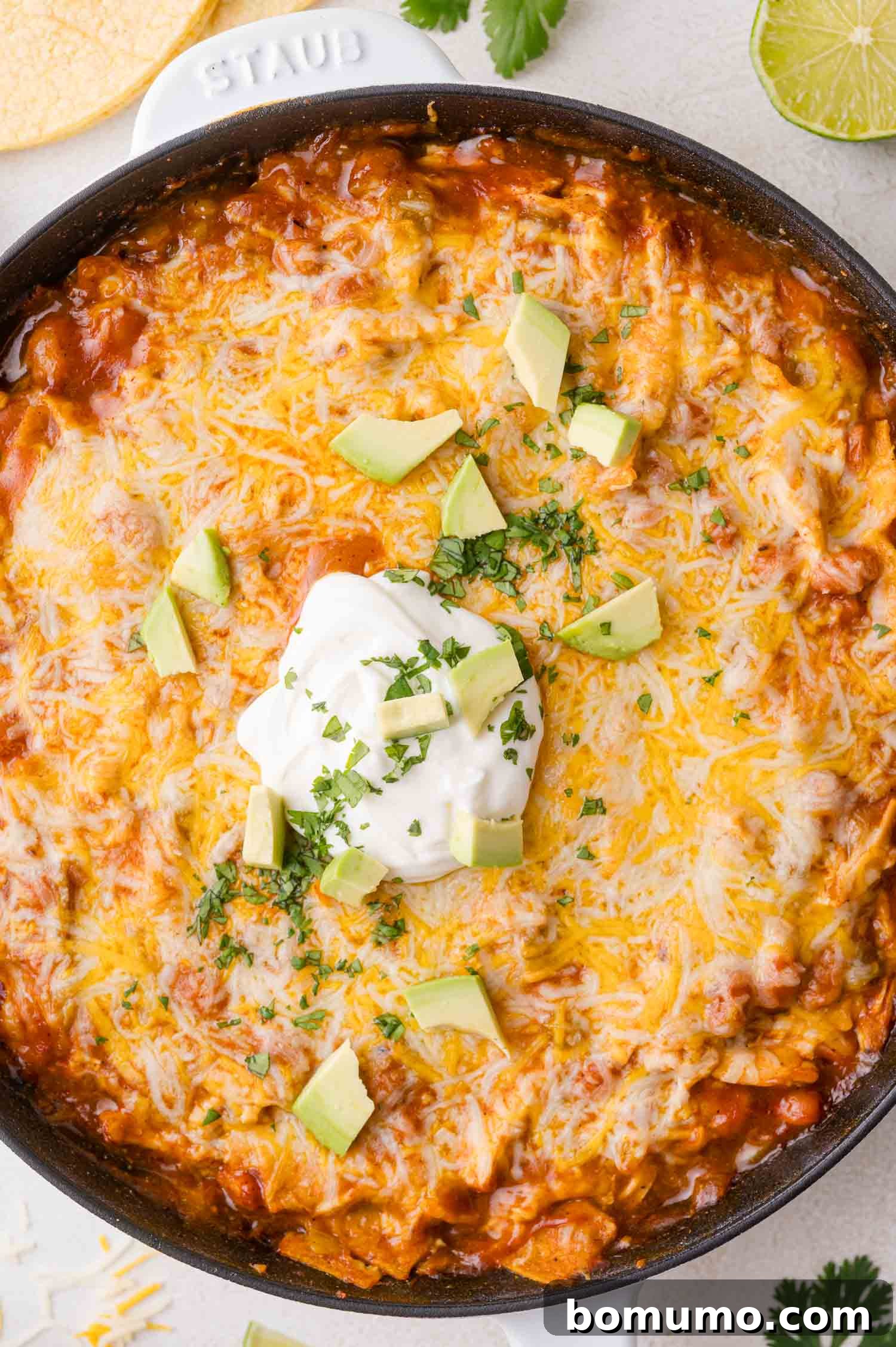 Quick Skillet Chicken Enchilada 2 A vibrant skillet filled with cheesy baked chicken enchilada casserole, generously topped with cool sour cream, fresh chopped cilantro, and creamy diced avocado, ready to serve.
