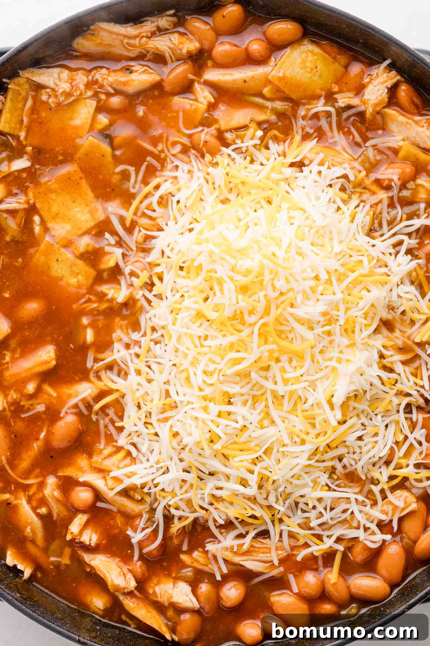 Quick Skillet Chicken Enchilada 12 A skillet filled with the rich enchilada mixture of shredded chicken, beans, and red sauce, now topped with a generous mound of shredded cheese, ready for baking.