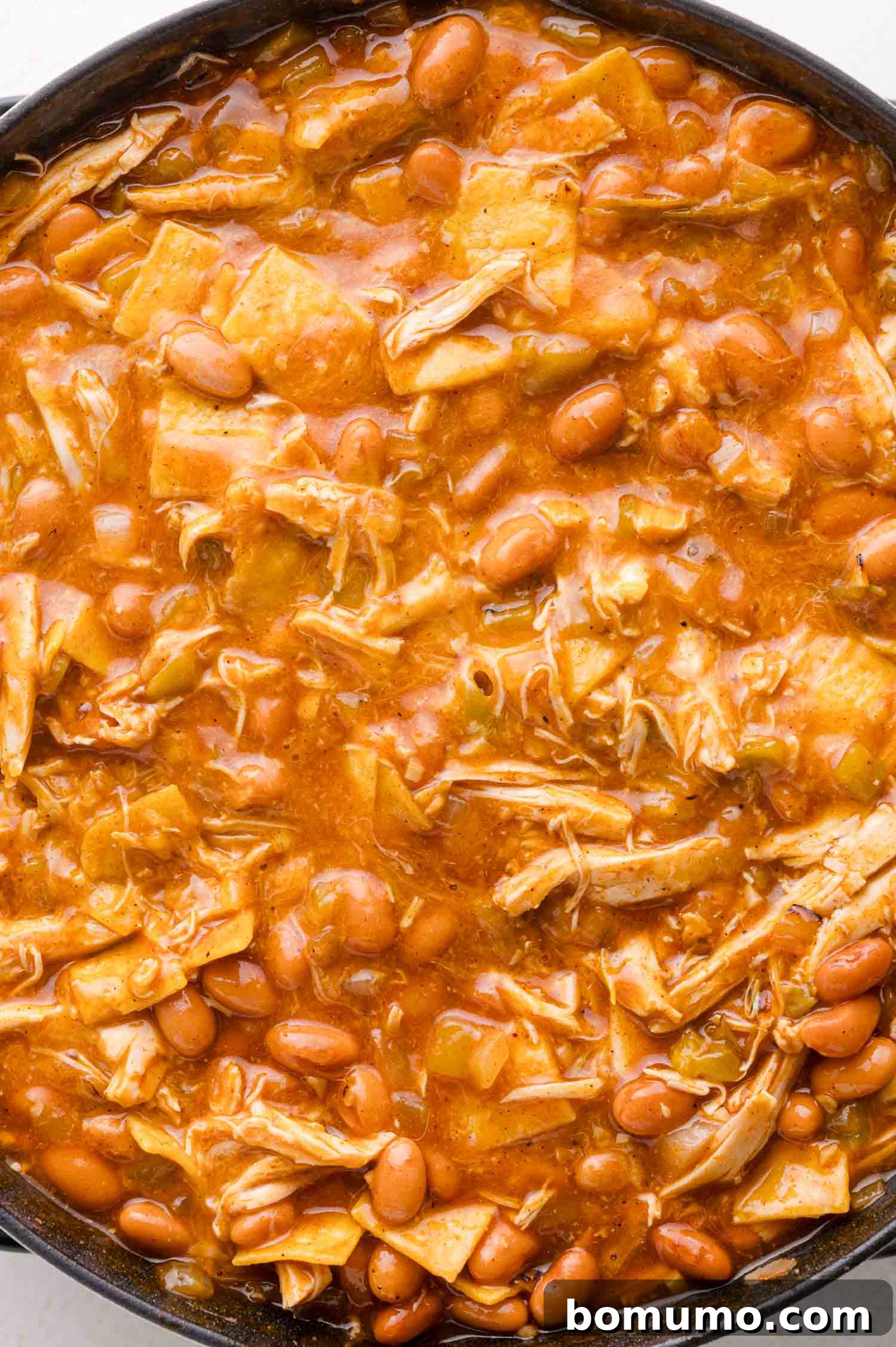 Quick Skillet Chicken Enchilada 13 A close-up of a pan brimming with chicken, pinto beans, tortilla pieces, and a rich red sauce, all integrated into a hearty mixture.