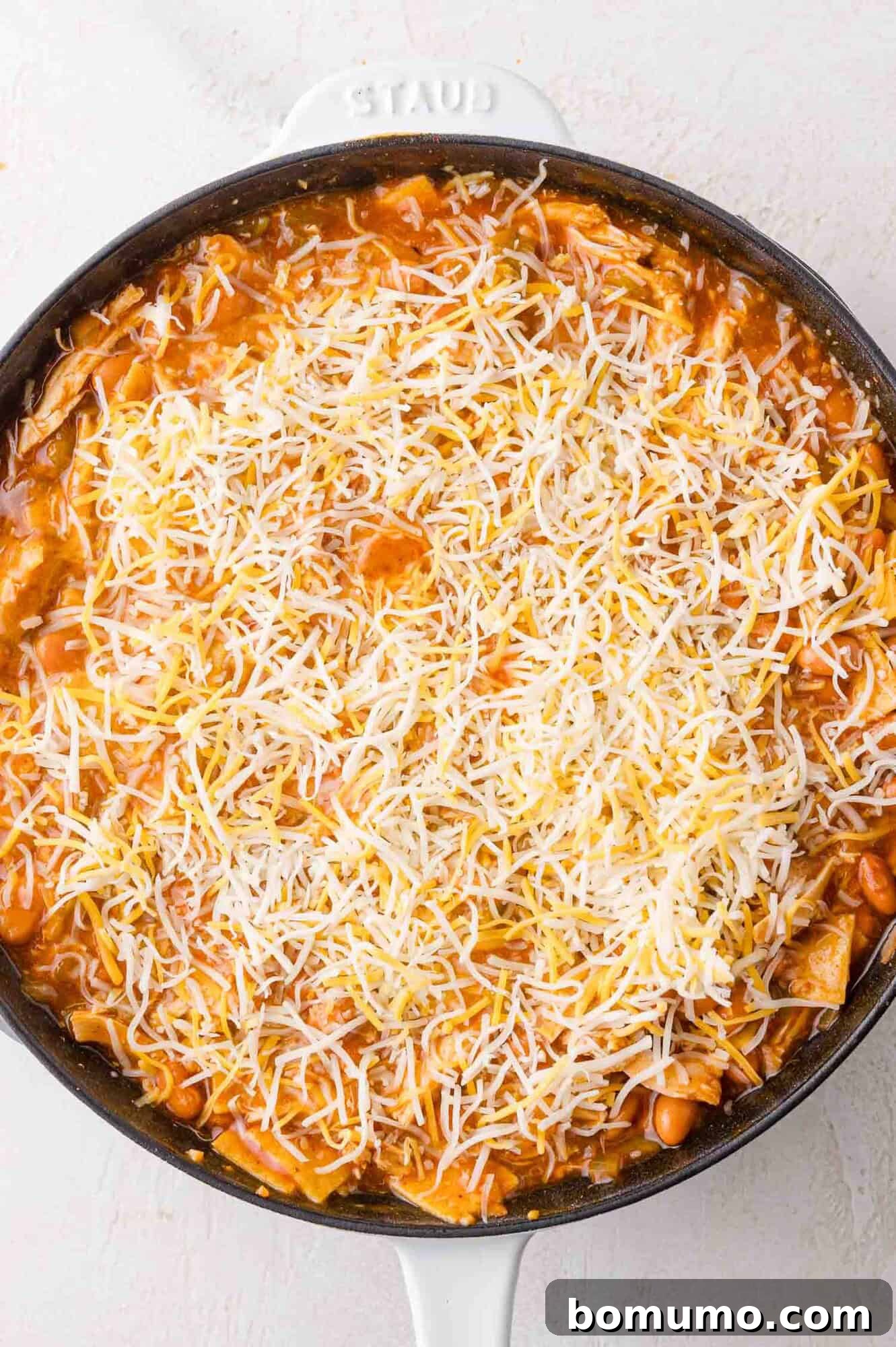 Quick Skillet Chicken Enchilada 14 A skillet filled with vibrant enchilada filling, evenly topped with shredded cheese, prepared and ready to be placed in the oven for baking.