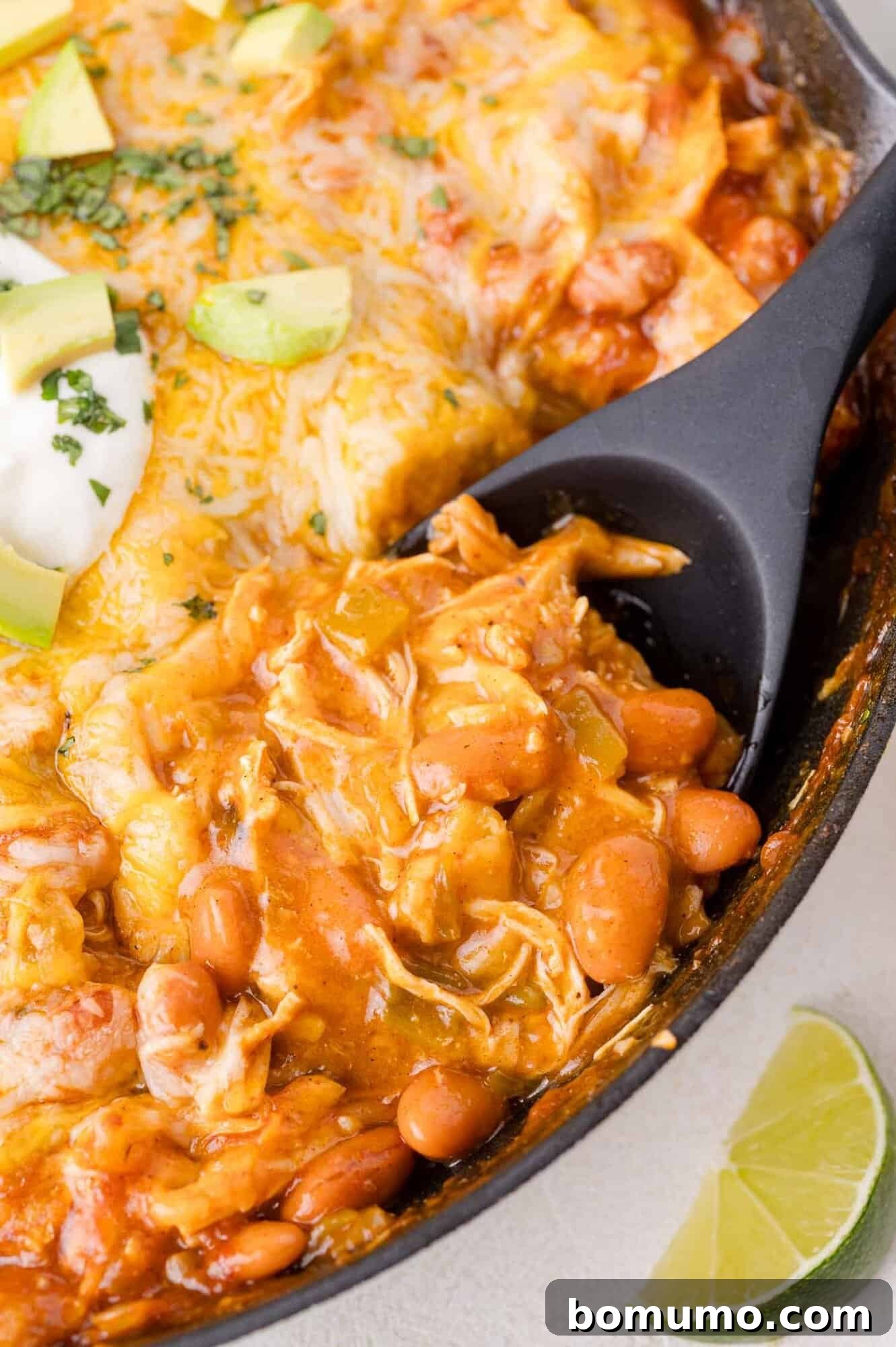 Quick Skillet Chicken Enchilada 16 Close-up of a skillet brimming with a rich, cheesy chicken enchilada casserole, generously topped with creamy avocado, cool sour cream, and fresh cilantro, with a bright lime wedge resting on the side, ready to be enjoyed.