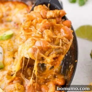 A serving of cheesy enchilada skillet being lifted from a casserole dish with a spoon, showing melted cheese stretching.