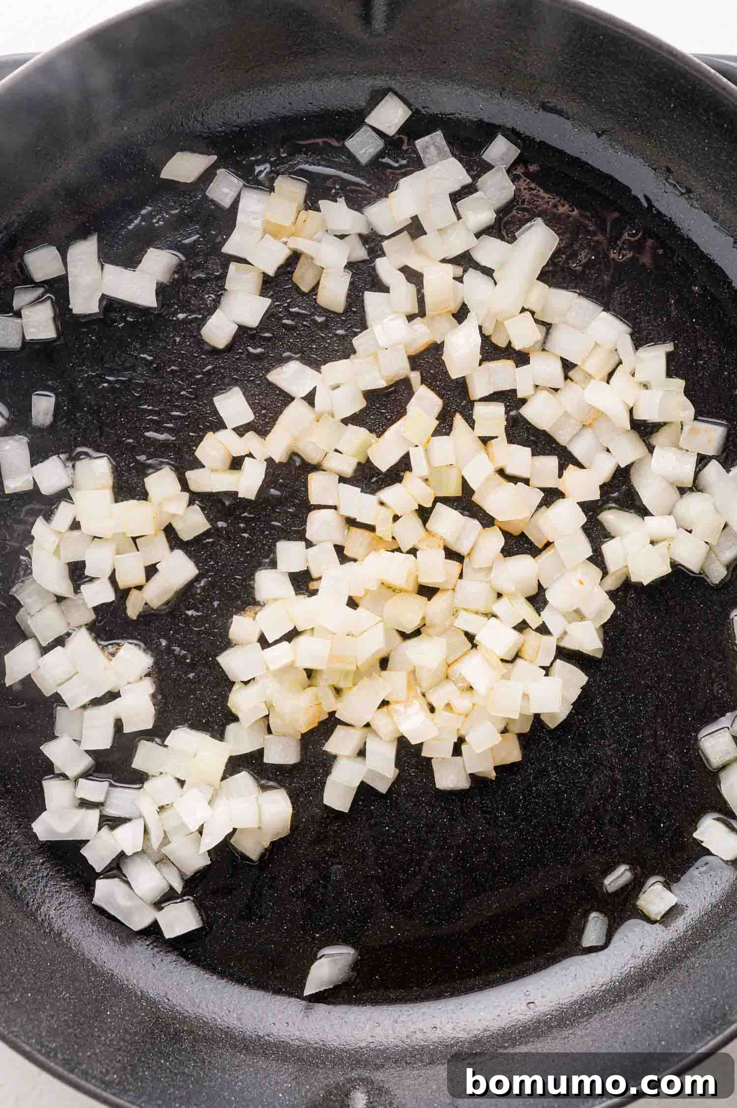 Quick Skillet Chicken Enchilada 5 Diced yellow onions cooking gently in a black skillet with a thin layer of olive oil, becoming translucent.