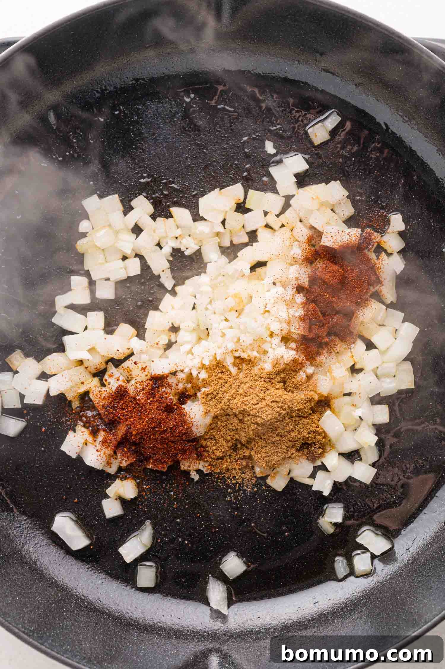 Quick Skillet Chicken Enchilada 7 Diced onions, minced garlic, and a blend of ground spices are being sautéed together in a black skillet, creating a rich aroma.