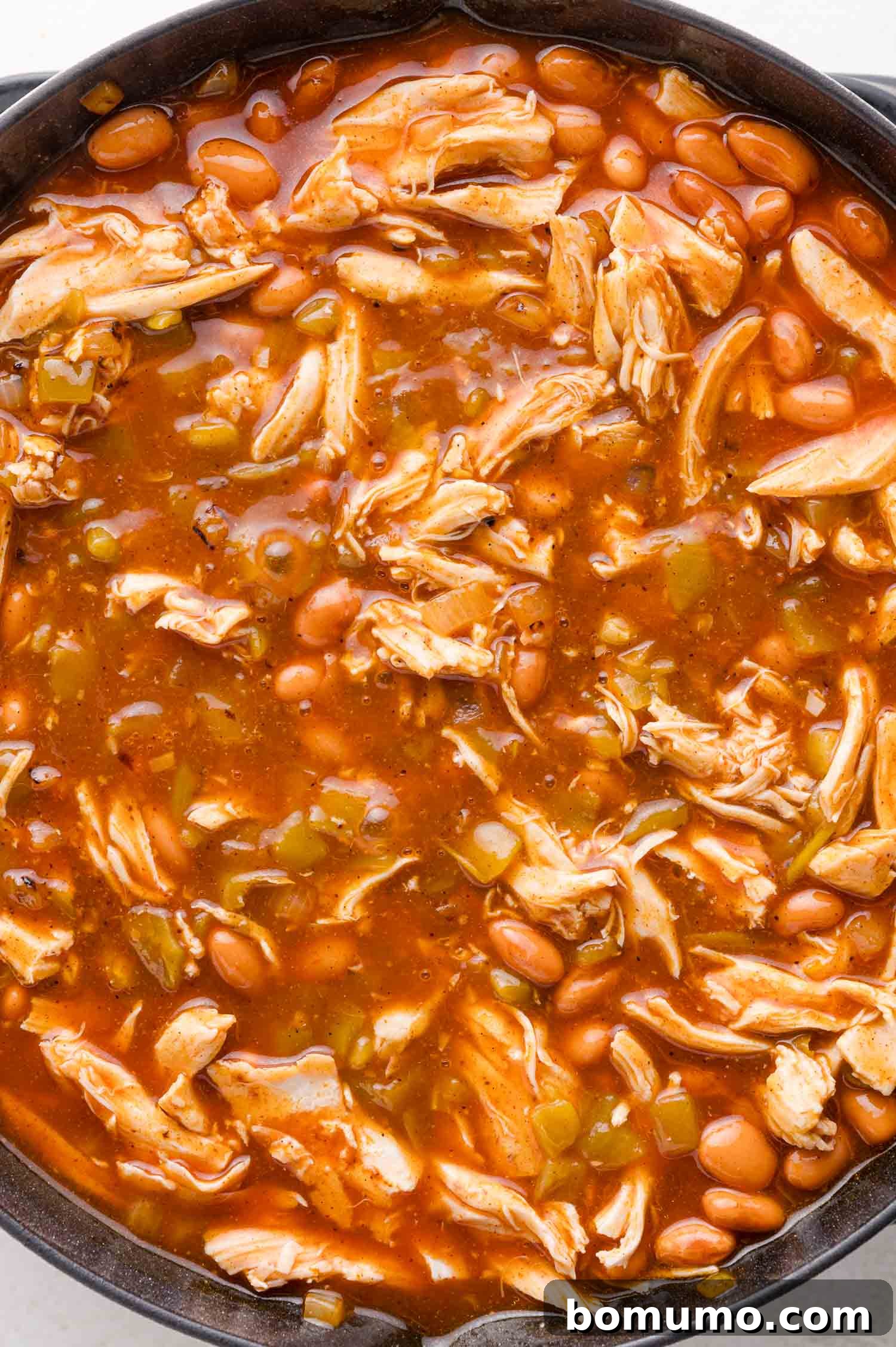 Quick Skillet Chicken Enchilada 9 A close-up of a pot filled with shredded chicken, pinto beans, and diced vegetables immersed in a rich red broth, simmering on the stove.