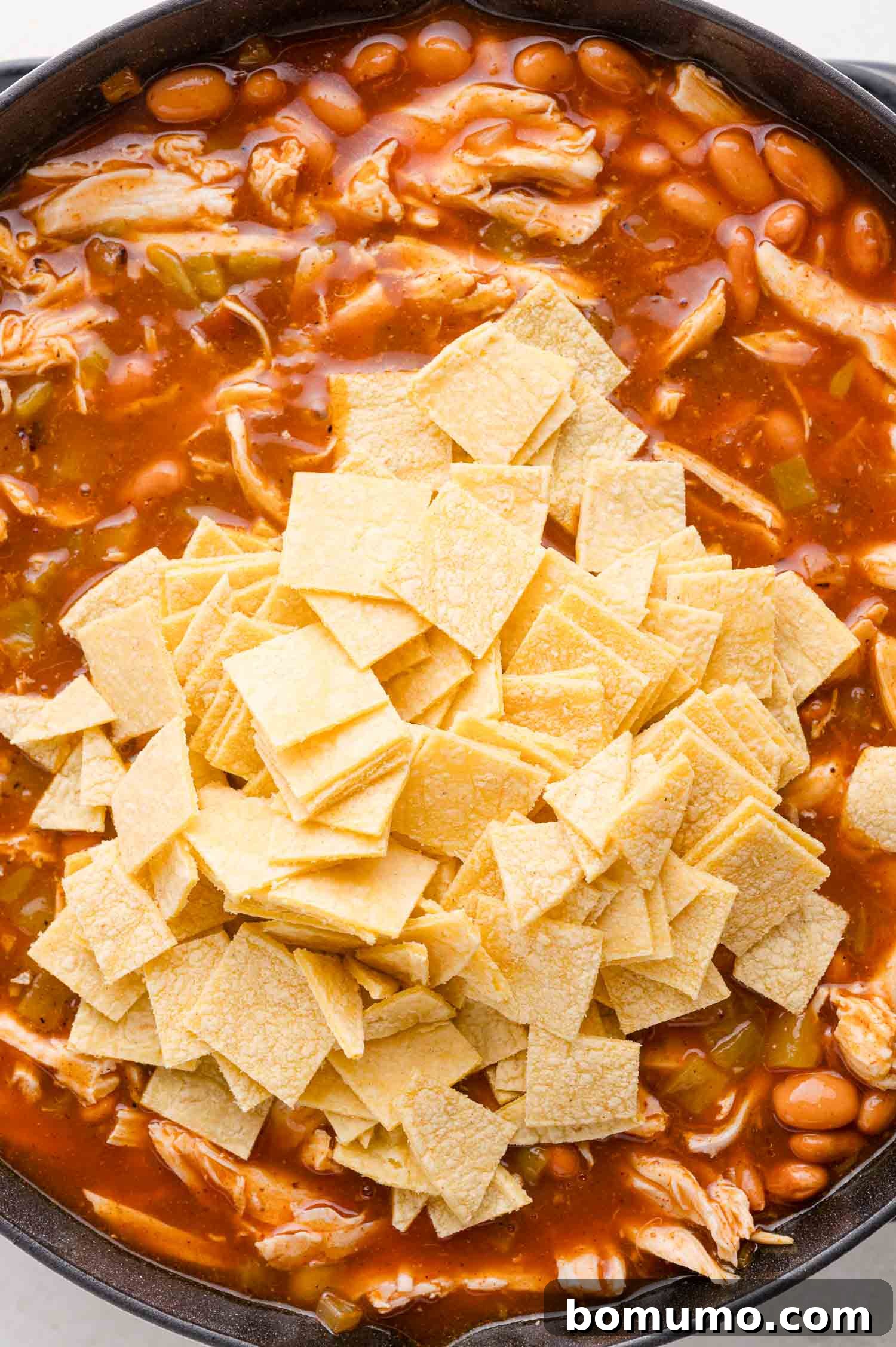 Quick Skillet Chicken Enchilada 10 A chicken enchilada skillet in a black pan with a mound of uncooked tortilla strips on top, ready to be mixed into the sauce and filling.