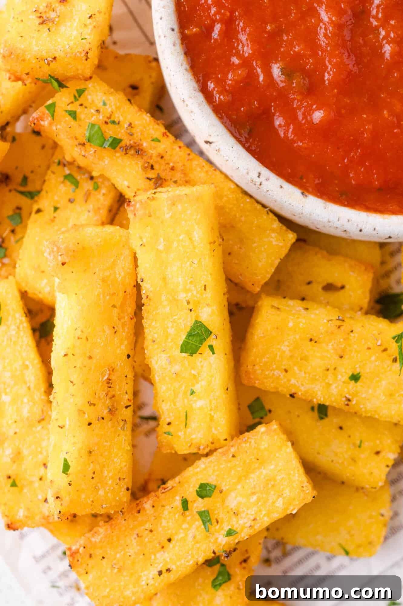Golden polenta fries garnished with herbs and a bowl of marinara sauce.