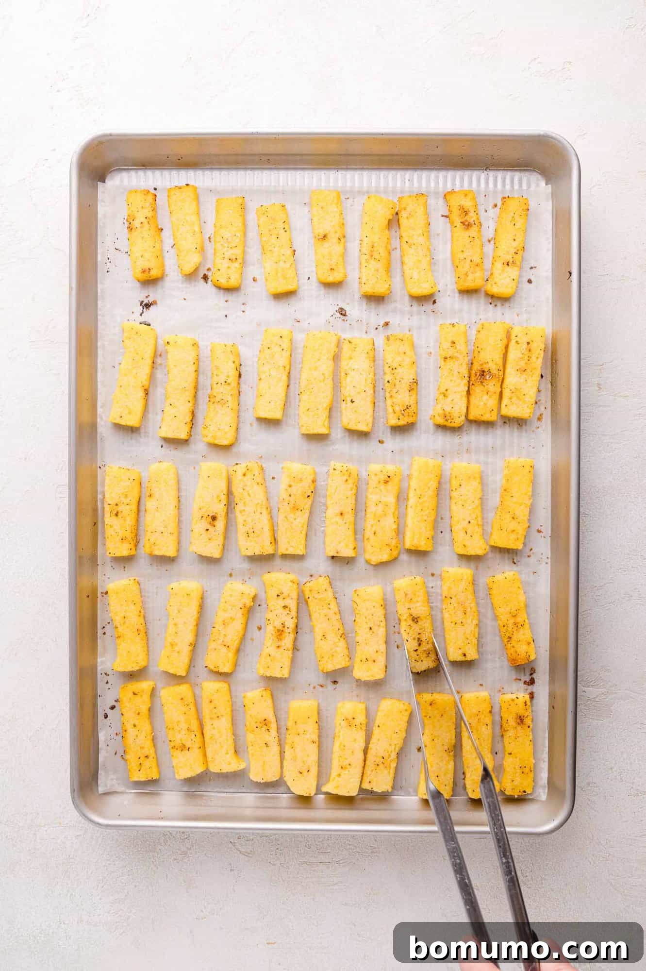 Polenta fries being arranged on a baking sheet.