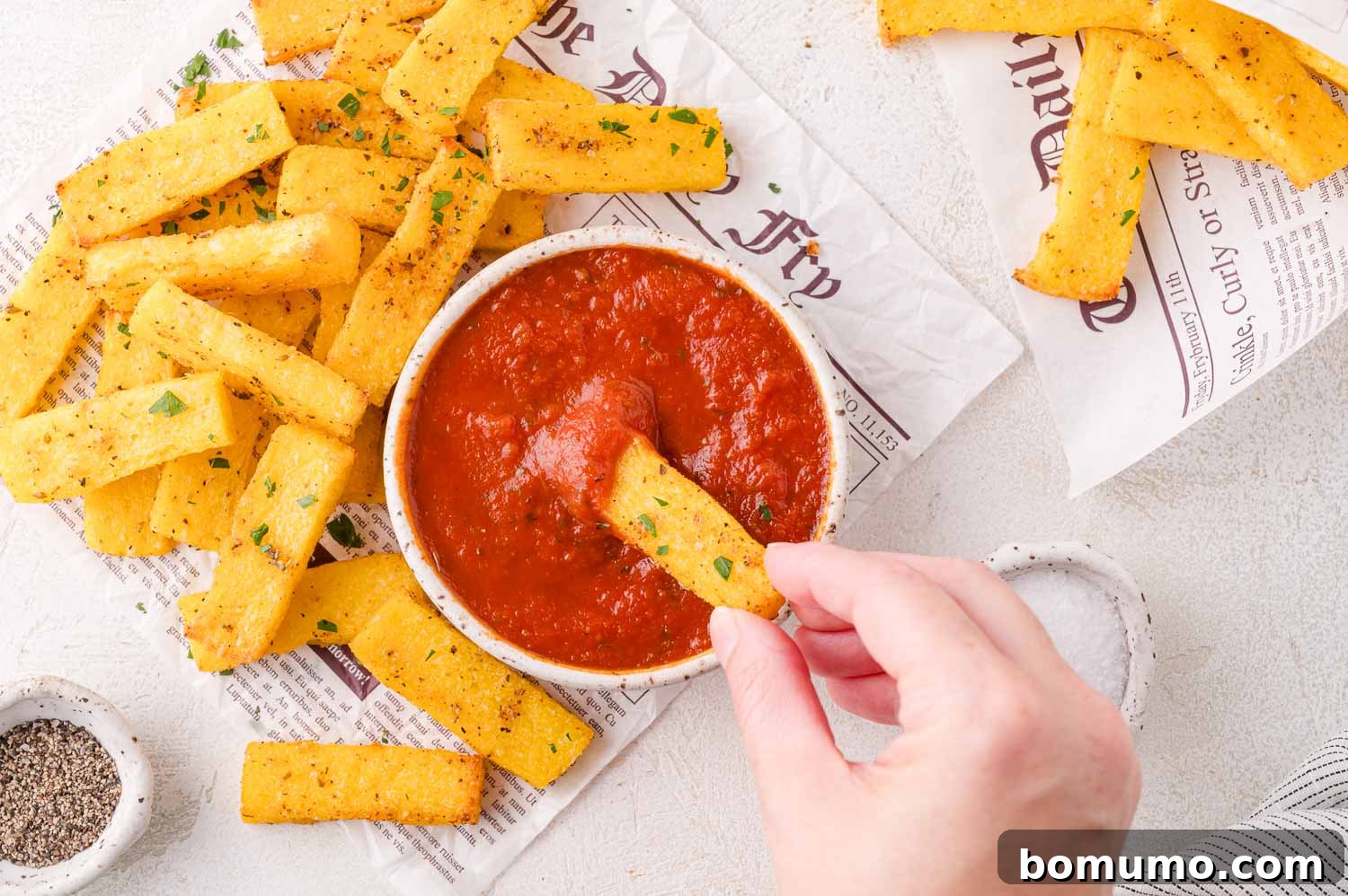 A hand dipping a polenta fry into marinara sauce.