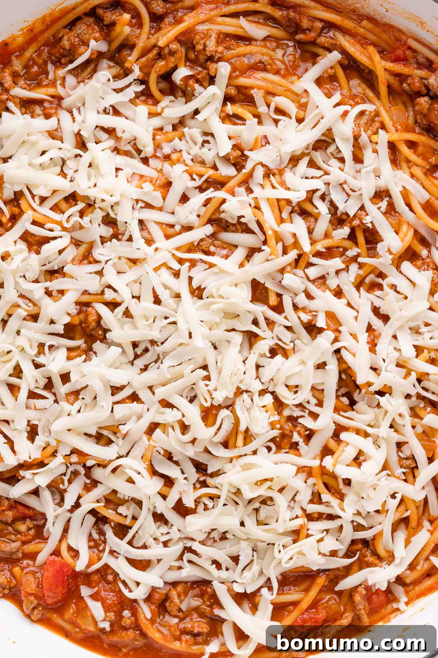 Cooked spaghetti generously mixed with savory ground beef and rich tomato sauce, all crowned with a delectable layer of freshly shredded mozzarella cheese, ready for melting.