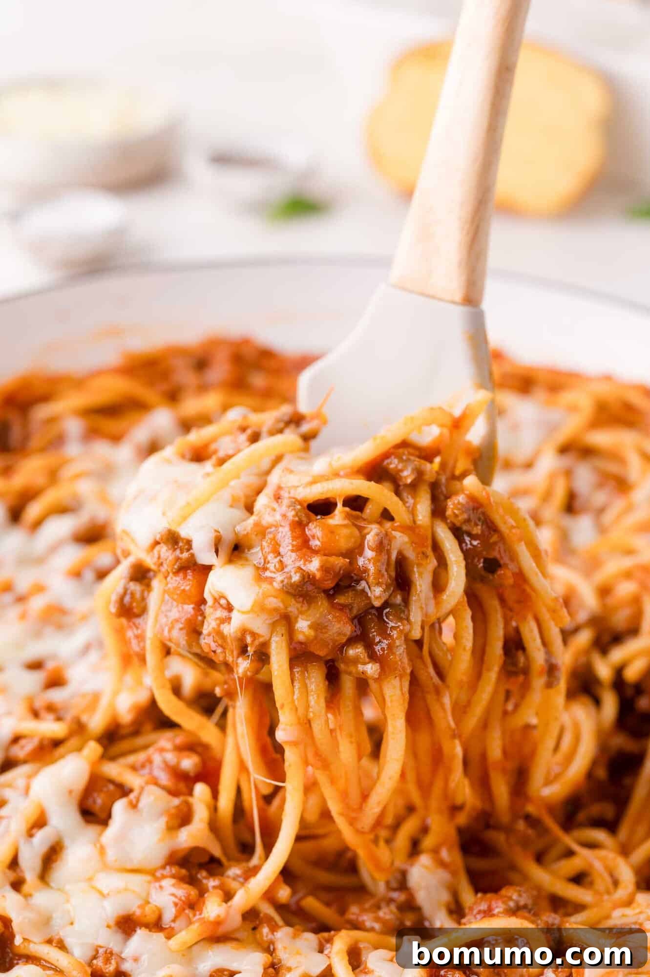 A white spatula gracefully lifts a perfect serving of one-pan spaghetti, showcasing the rich ground meat sauce and tantalizing melted cheese, straight from the pan.