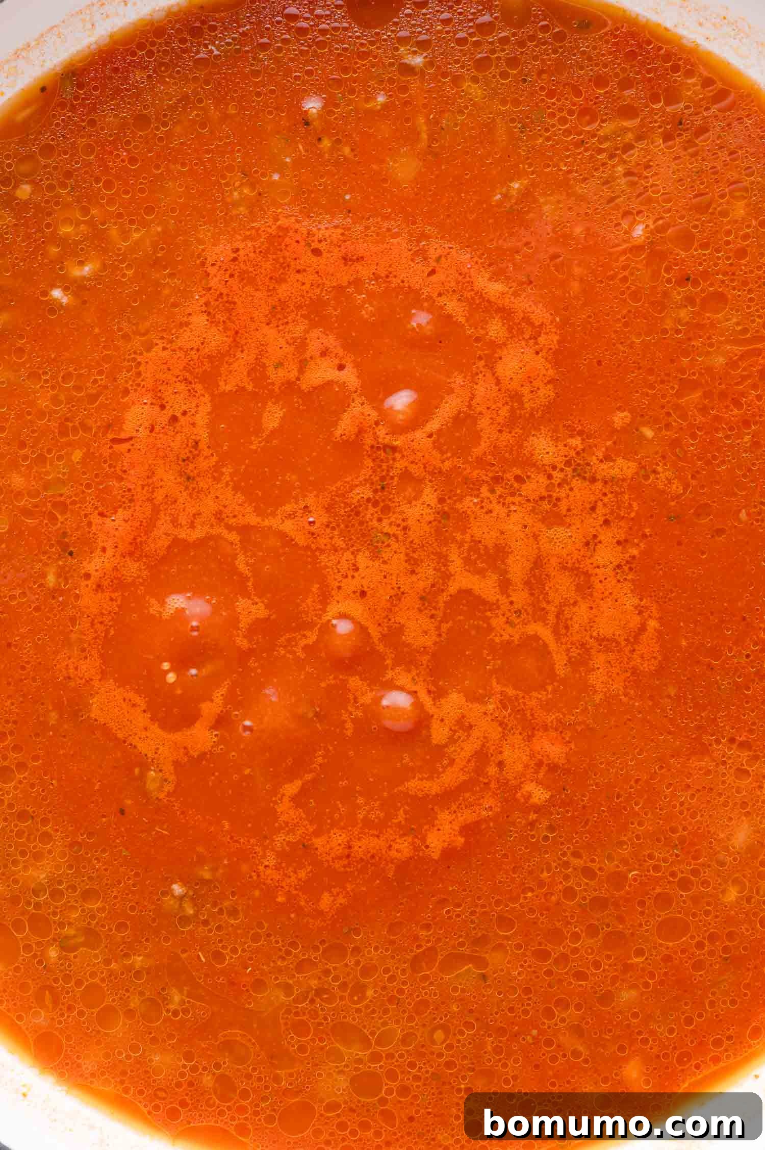 A close-up shot of a rich, red tomato sauce simmering gently in a bowl, showcasing its smooth texture and a few tiny bubbles on its slightly oily surface.