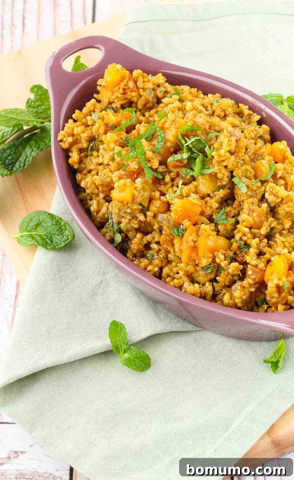 Moroccan freekeh with apricots in a purple dish, garnished with fresh mint.