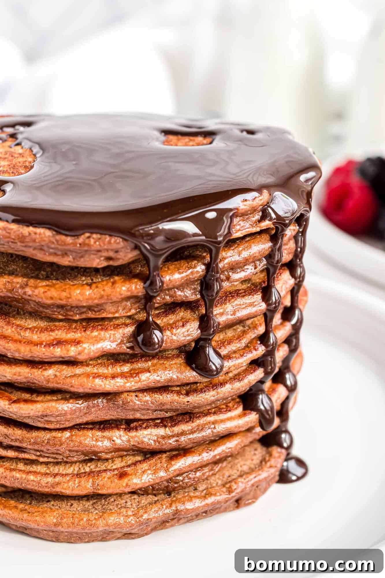 A tall stack of fluffy chocolate pancakes, generously topped with chocolate syrup, ready to be devoured.