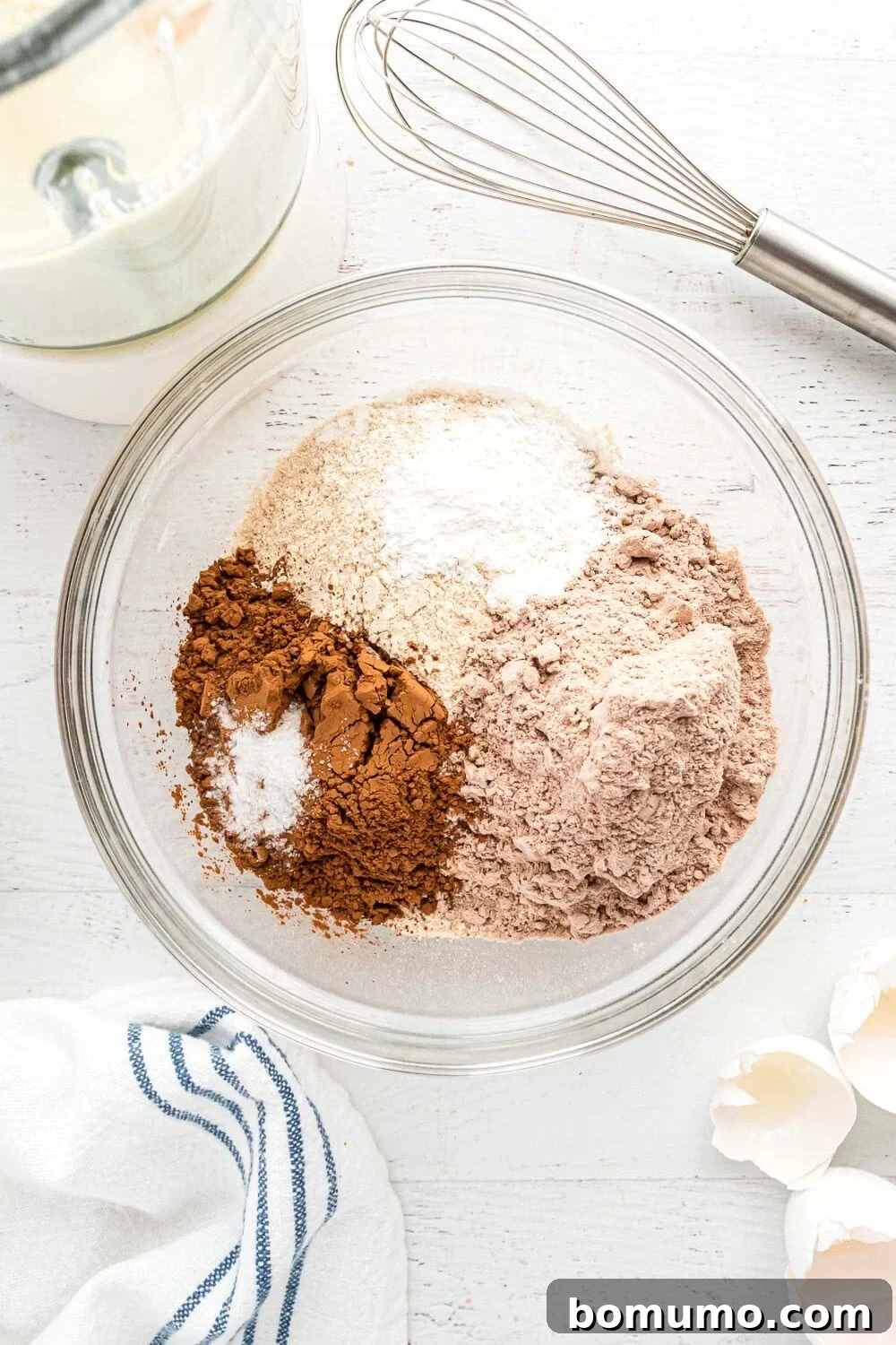 Dry ingredients (flour, protein powder, cocoa, baking powder, salt) layered on top of wet ingredients in a blender.