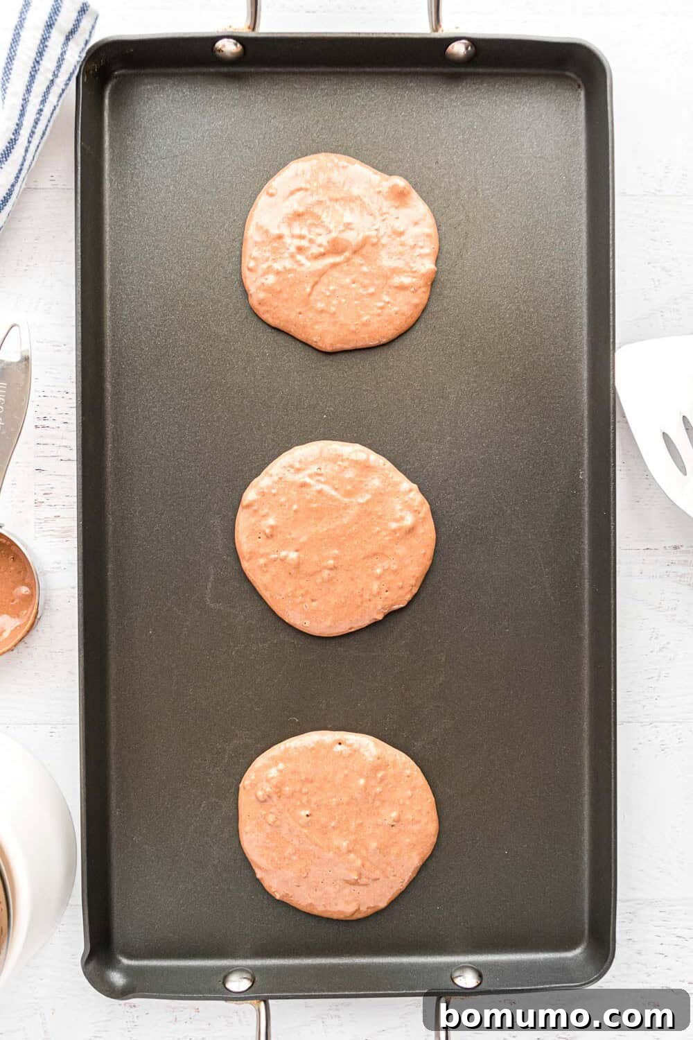 Freshly poured pancake batter cooking on a hot griddle, bubbles forming.