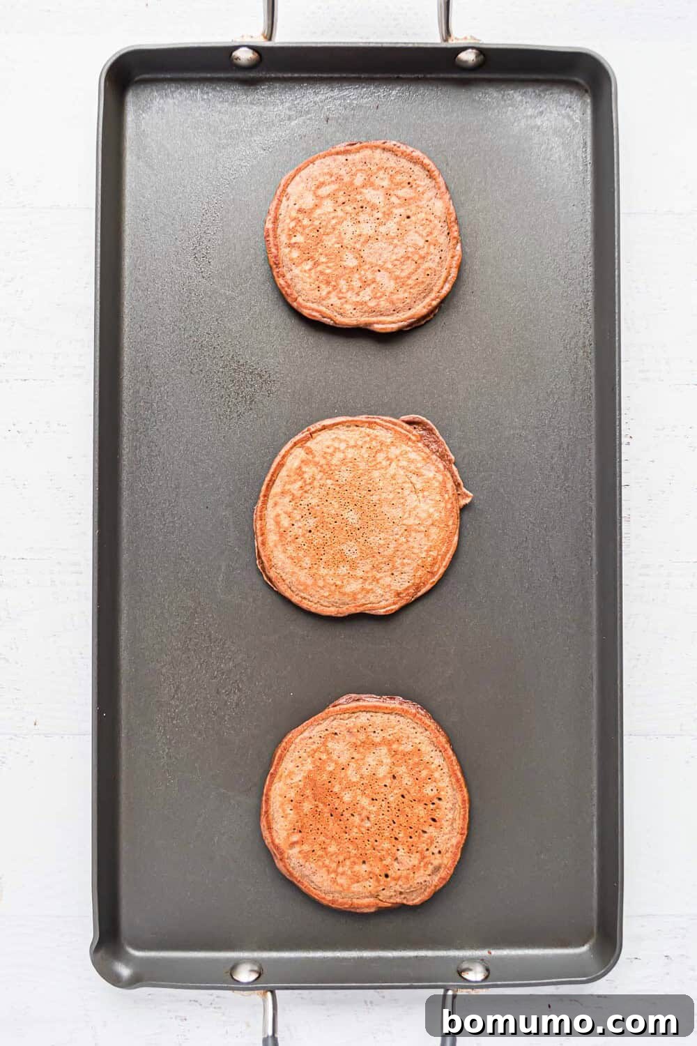 Golden brown chocolate protein pancakes cooking on a griddle, almost ready to serve.