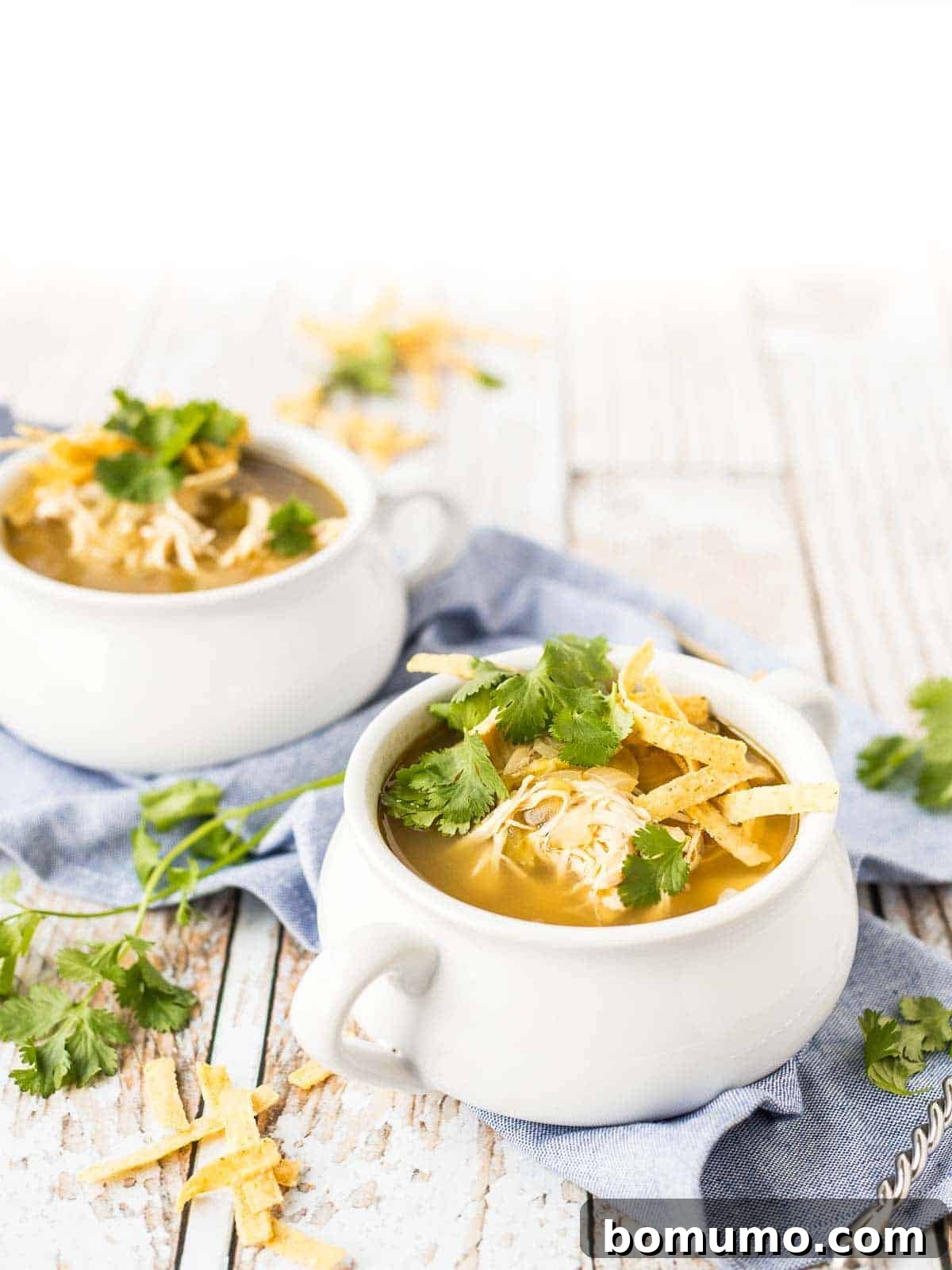 Two white soup bowls with handles, filled to the brim with creamy chicken enchilada soup, ready to be served and enjoyed.
