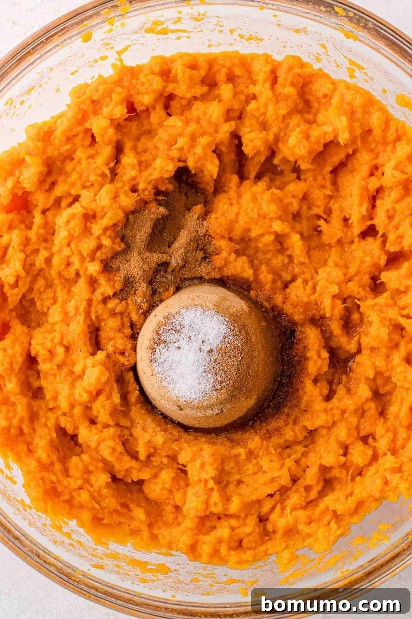 Brown sugar, vanilla, and spices freshly added to a bowl of mashed sweet potatoes, arranged neatly before being mixed in, showcasing all ingredients ready for blending.