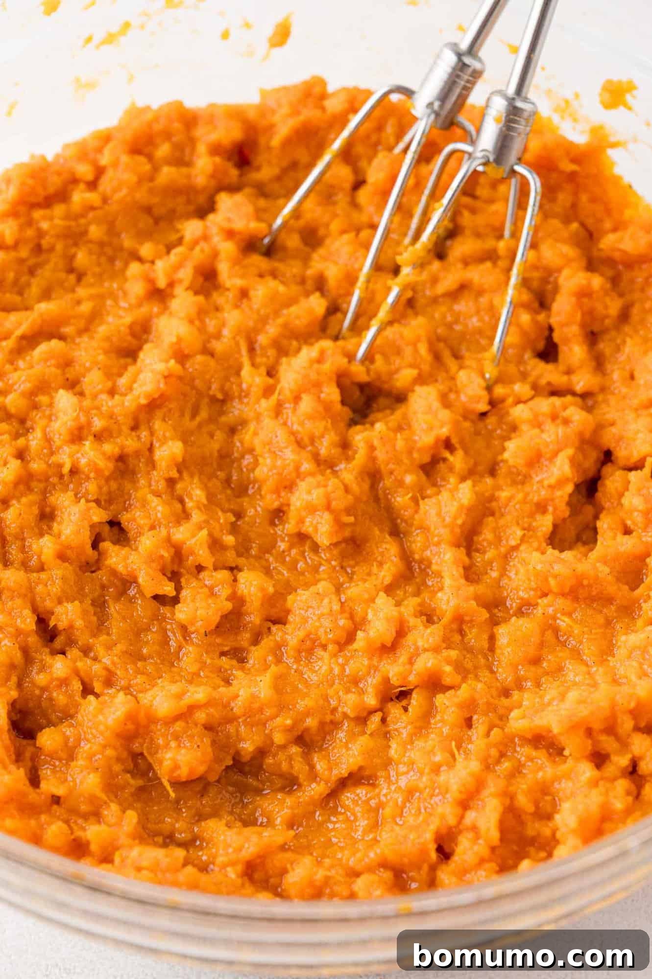 The mashed sweet potatoes fully blended with brown sugar and spices, with the electric mixer beaters still in the bowl, indicating a smooth and ready mixture.
