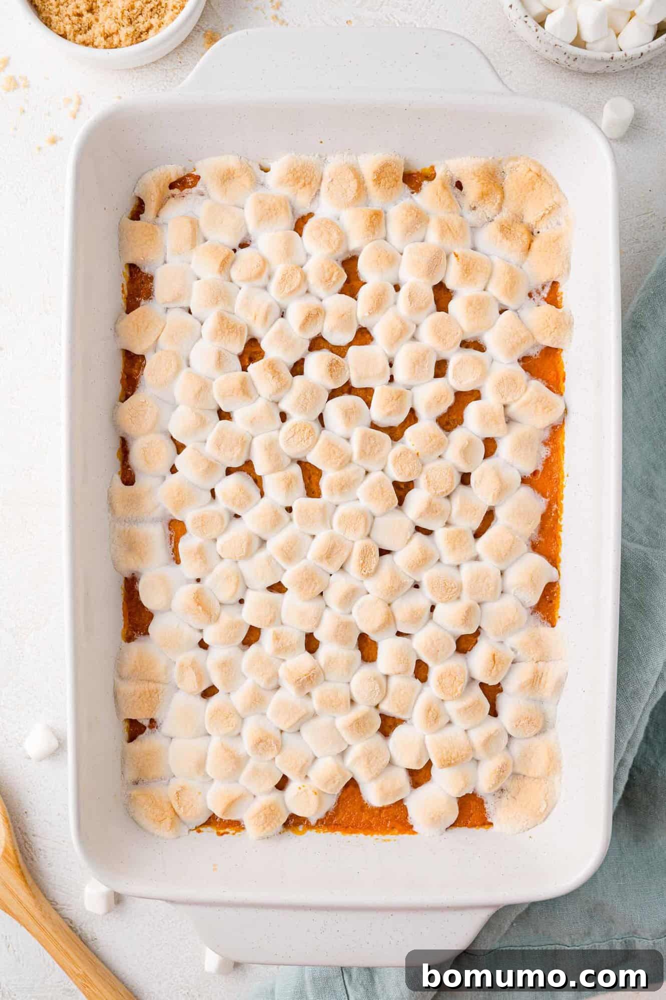 A fully baked sweet potato casserole, still in its dish, showcasing a glistening, perfectly toasted layer of golden-brown marshmallows, ready to be served.