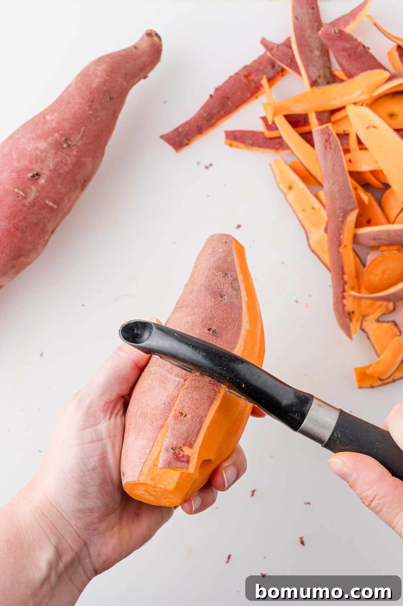A hand expertly peeling the skin from a sweet potato, revealing the vibrant orange flesh beneath, signifying the start of the preparation process.