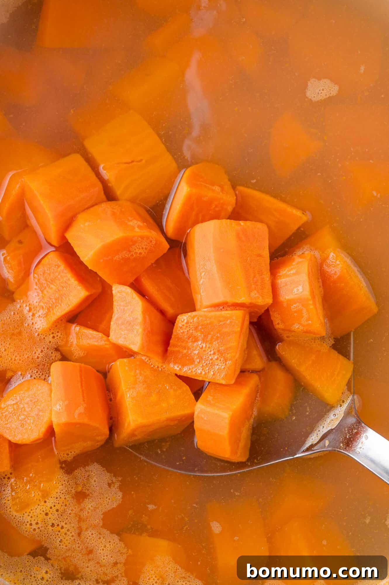 A slotted spoon carefully lifting cooked sweet potato chunks from boiling water, demonstrating their readiness for mashing and highlighting proper drainage.