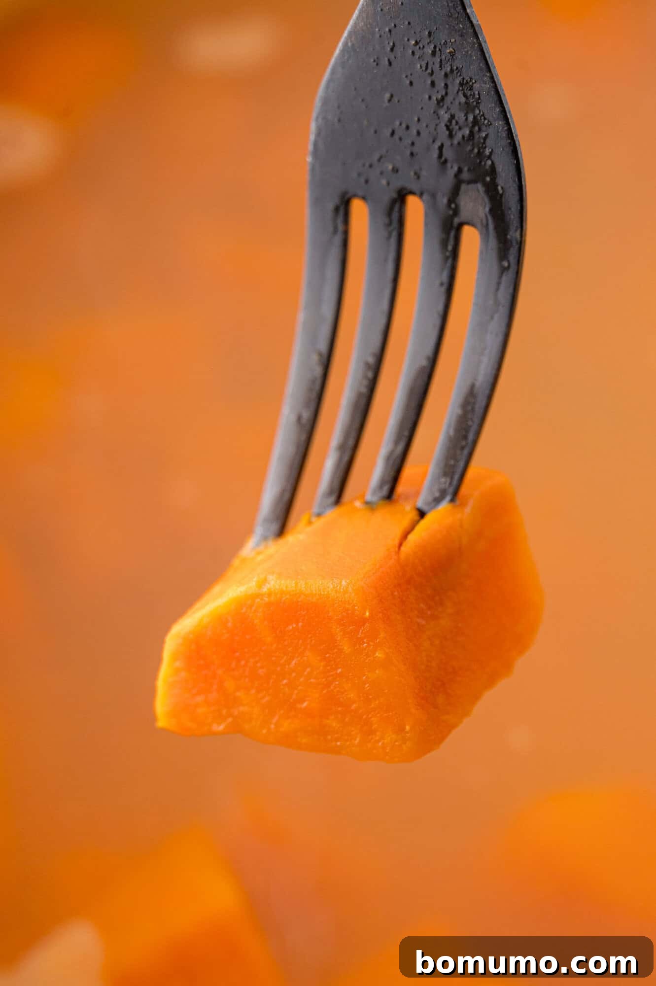 A fork effortlessly piercing a sweet potato chunk, illustrating its perfect tenderness after cooking and confirming its readiness for mashing.