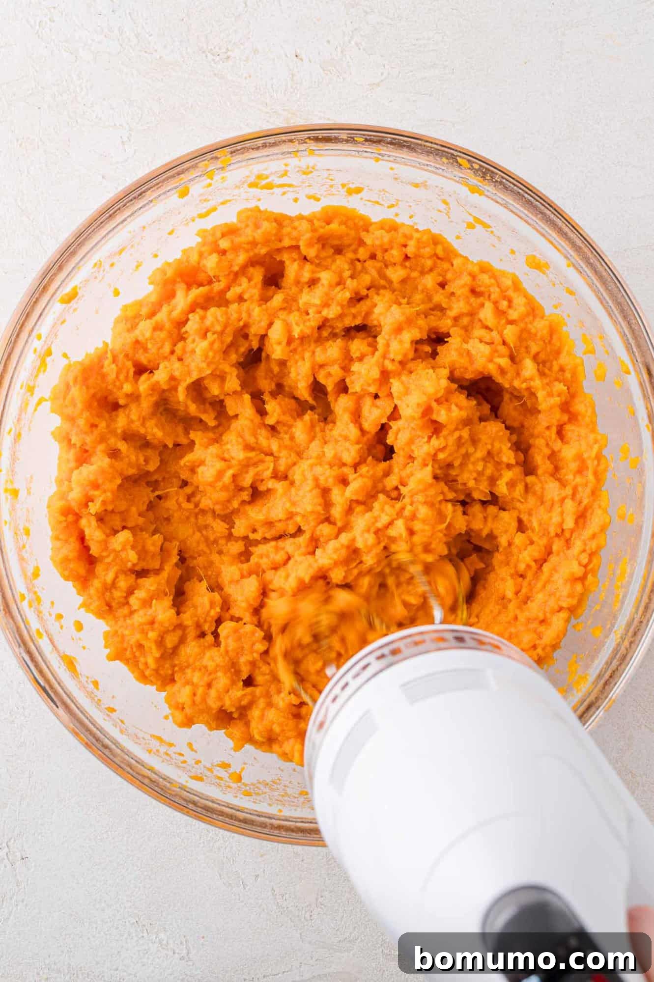 An electric mixer in action, diligently mashing sweet potatoes and butter in a bowl, creating a smooth and creamy consistency.