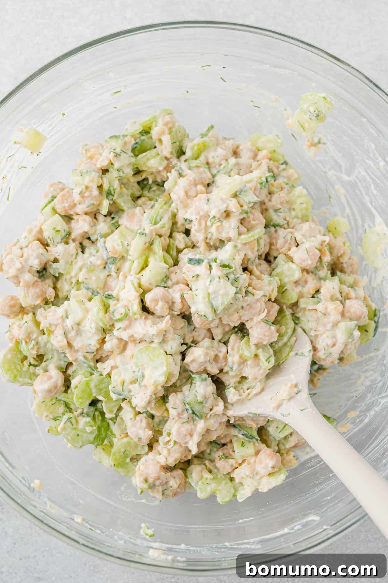 The vibrant mixture of vegetables being carefully folded into the creamy chickpea salad base.