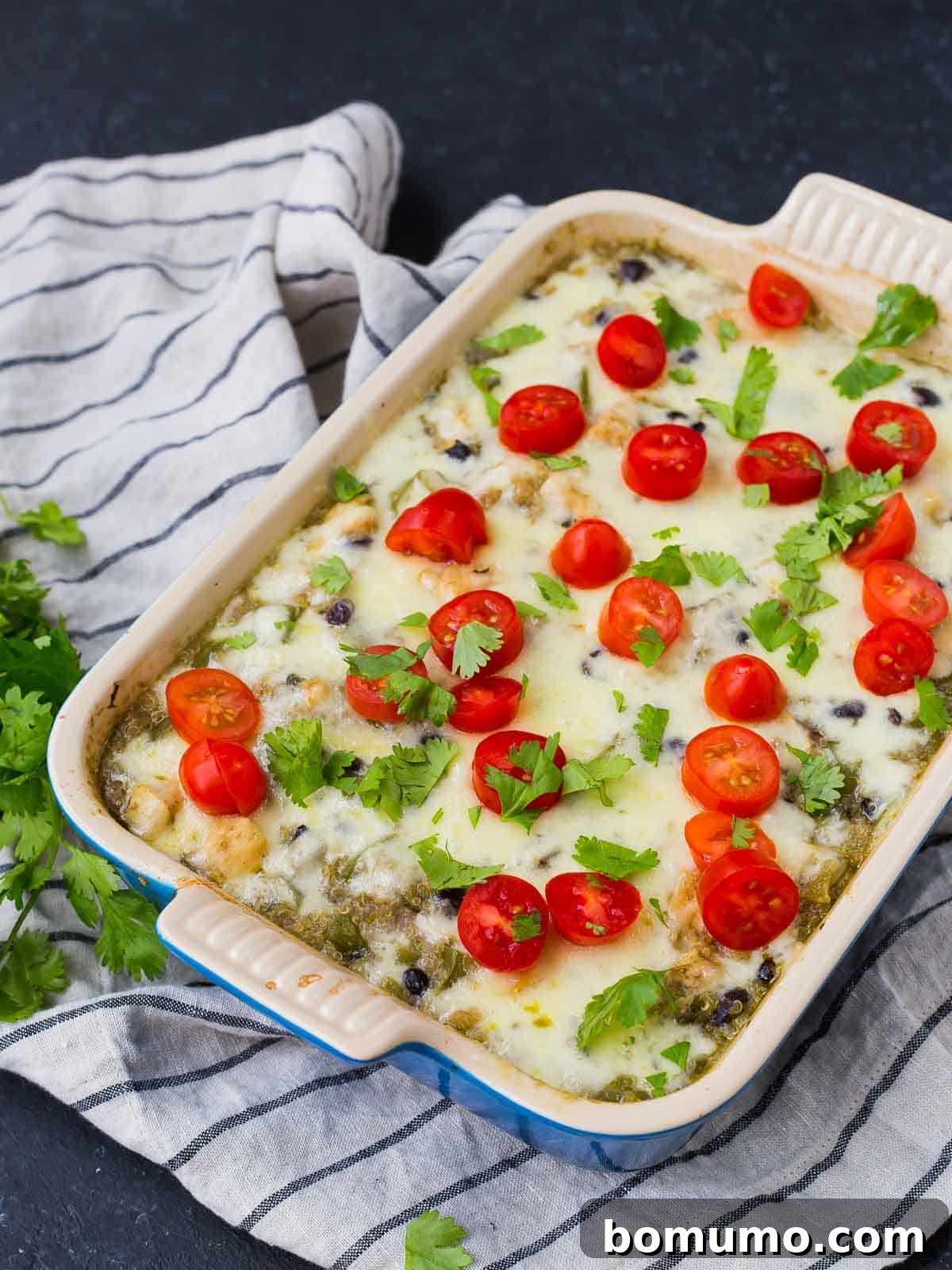 Overhead shot of a square baking dish filled with casserole, garnished with halved cherry tomatoes and fresh herbs.