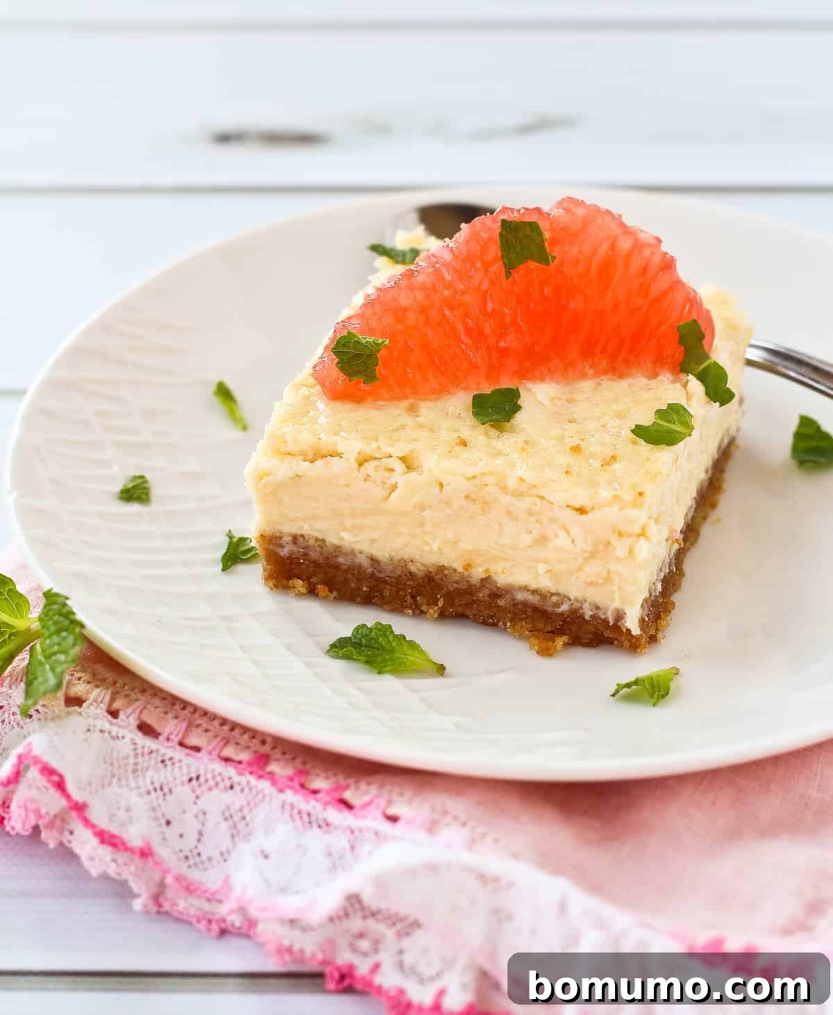 A perfectly sliced grapefruit cheesecake bar, showcasing its golden crust, creamy filling, and a fresh grapefruit slice garnish.