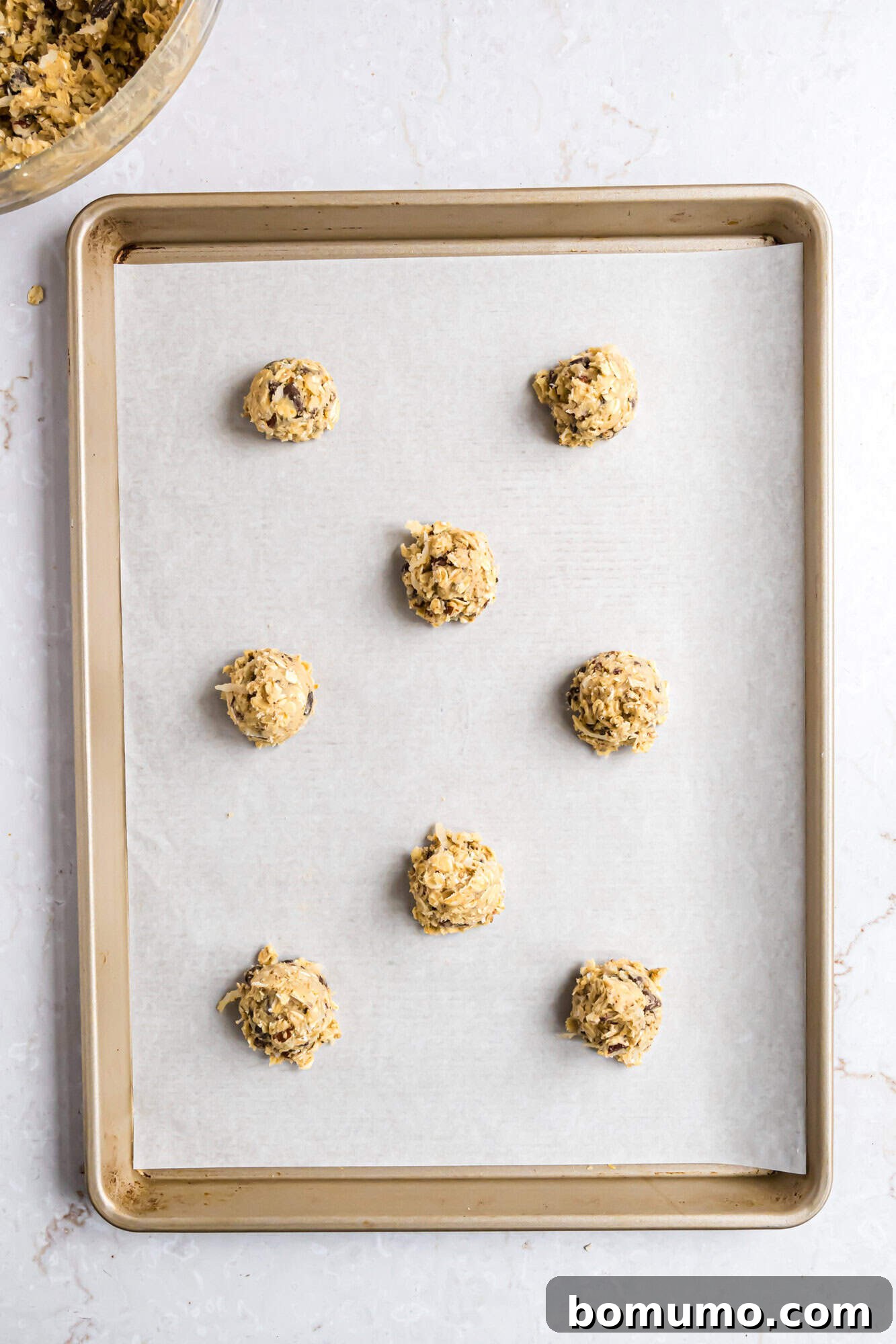 A baking sheet lined with parchment paper holds eight evenly spaced scoops of unbaked cookie dough.