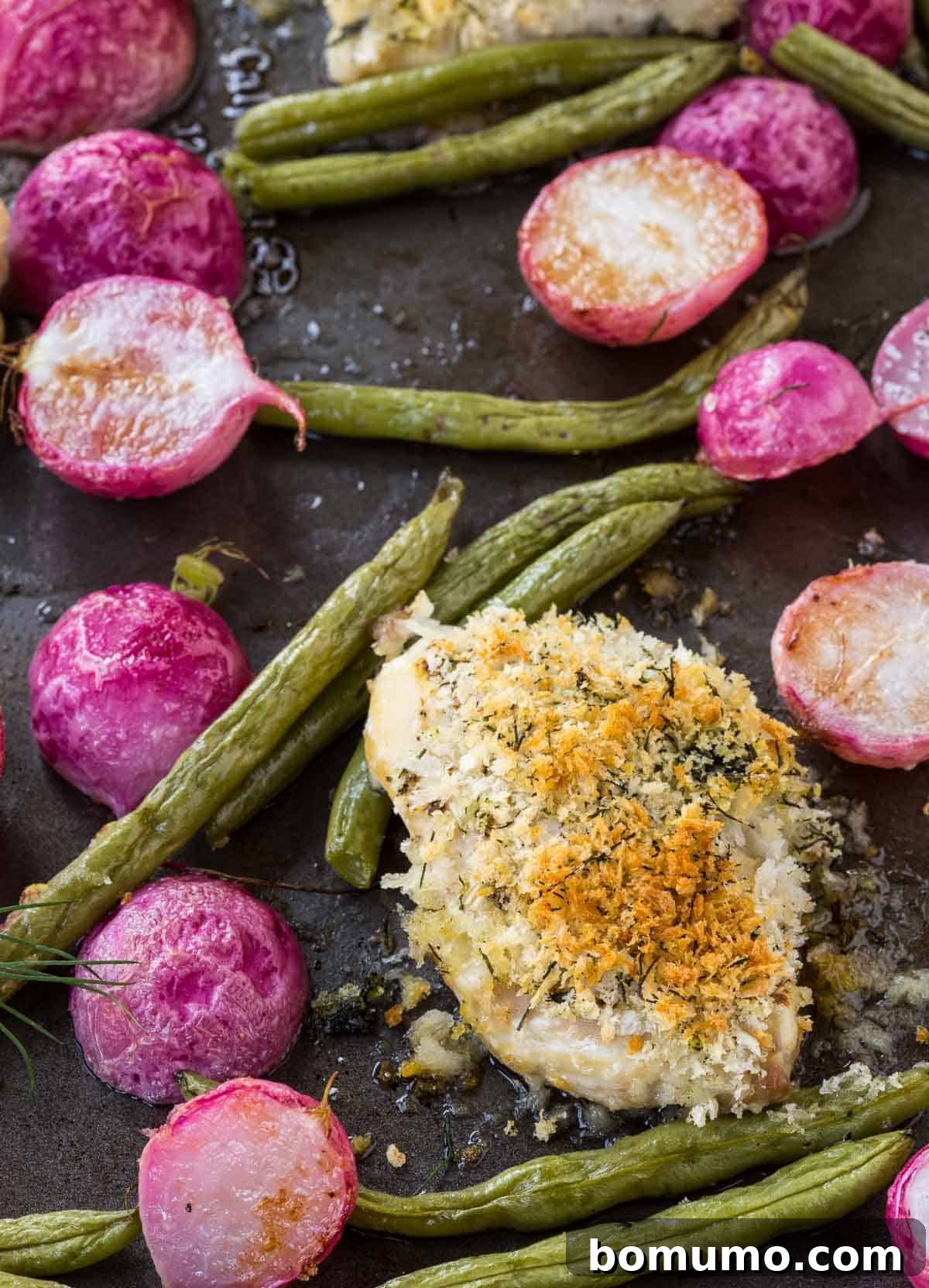 Close-up of perfectly roasted crispy Dijon dill chicken thighs alongside vibrant green beans and tender radishes on a sheet pan, ready to be served.