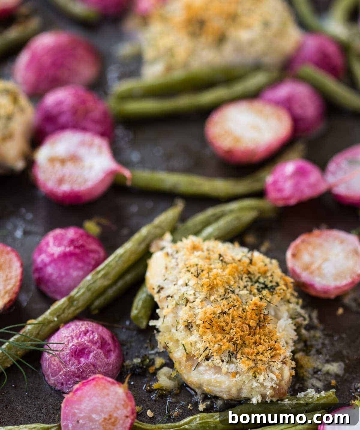 Overhead view of a sheet pan filled with golden-brown chicken thighs, vibrant green beans, and roasted radishes, showcasing a complete and appetizing meal.