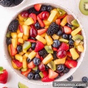 A bowl filled with a delightful mixed fruit salad featuring vibrant strawberries, plump blueberries, dark blackberries, golden pineapple, tangy kiwi, and sweet grapes, all glistening with a fresh dressing.