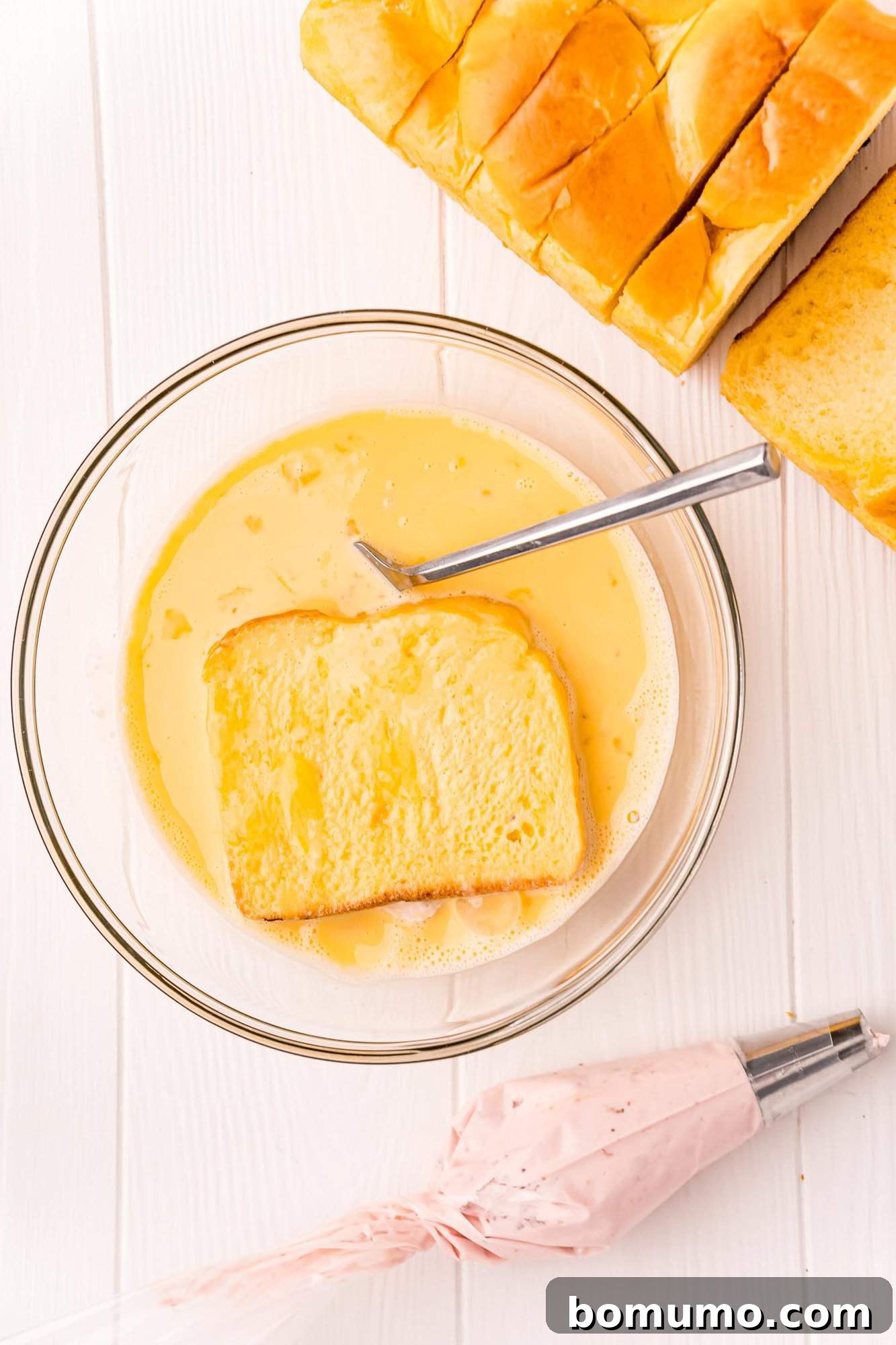 The stuffed brioche bread slice, now flipped, soaking up the egg mixture on its second side, ensuring full saturation.