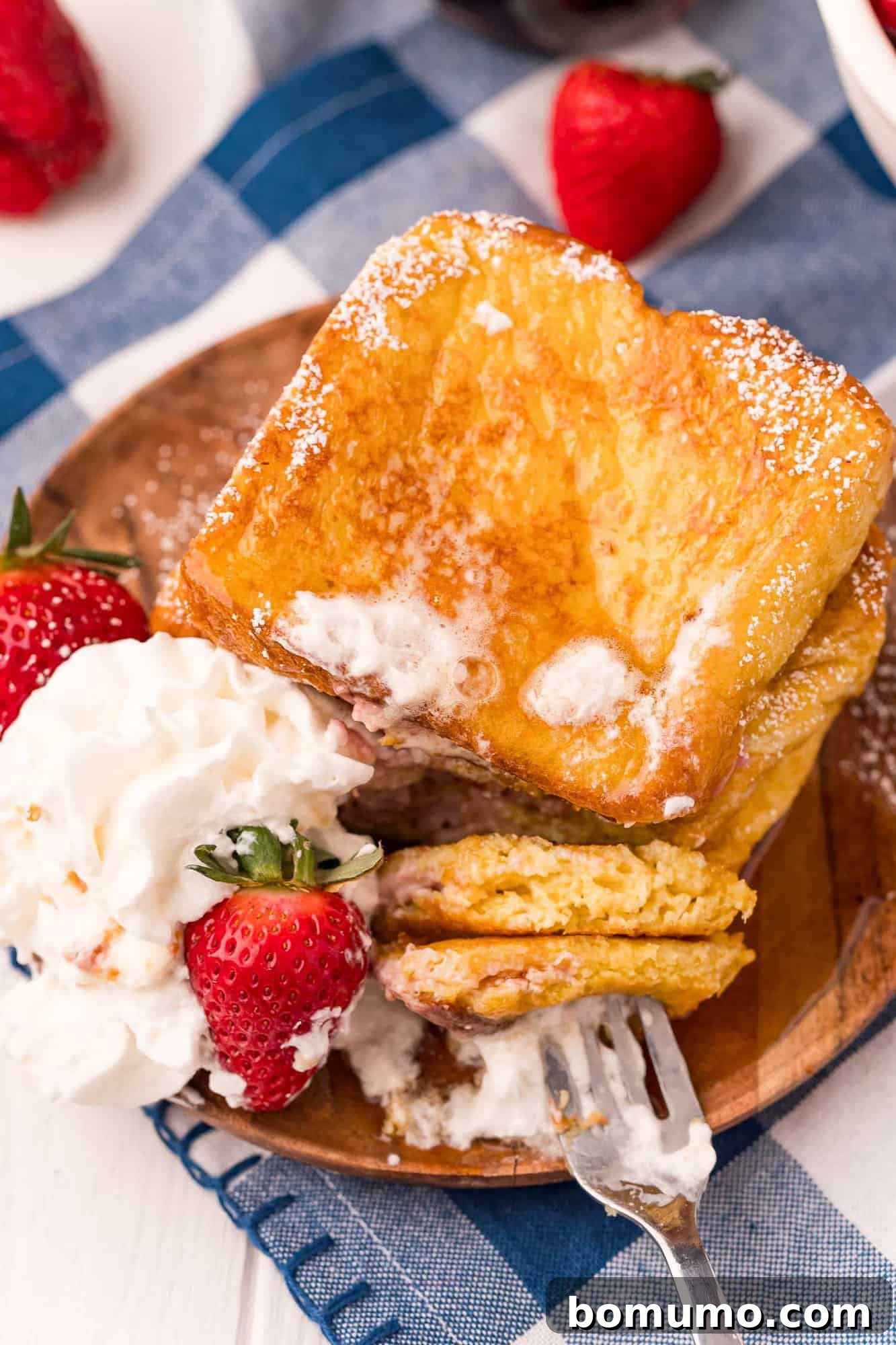 A slice of stuffed french toast, cut in half to showcase the warm, gooey strawberry cream cheese filling.