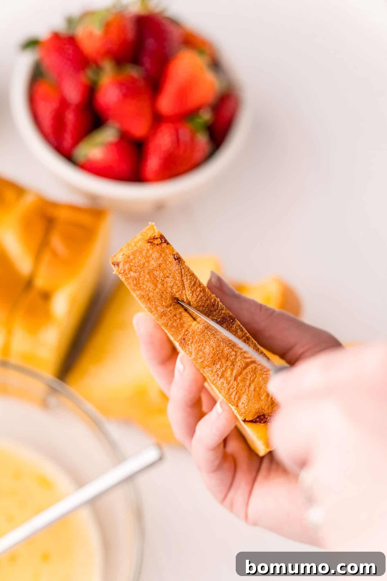 A sharp knife carefully cutting a slit into a thick slice of brioche bread, creating a pocket for the filling.